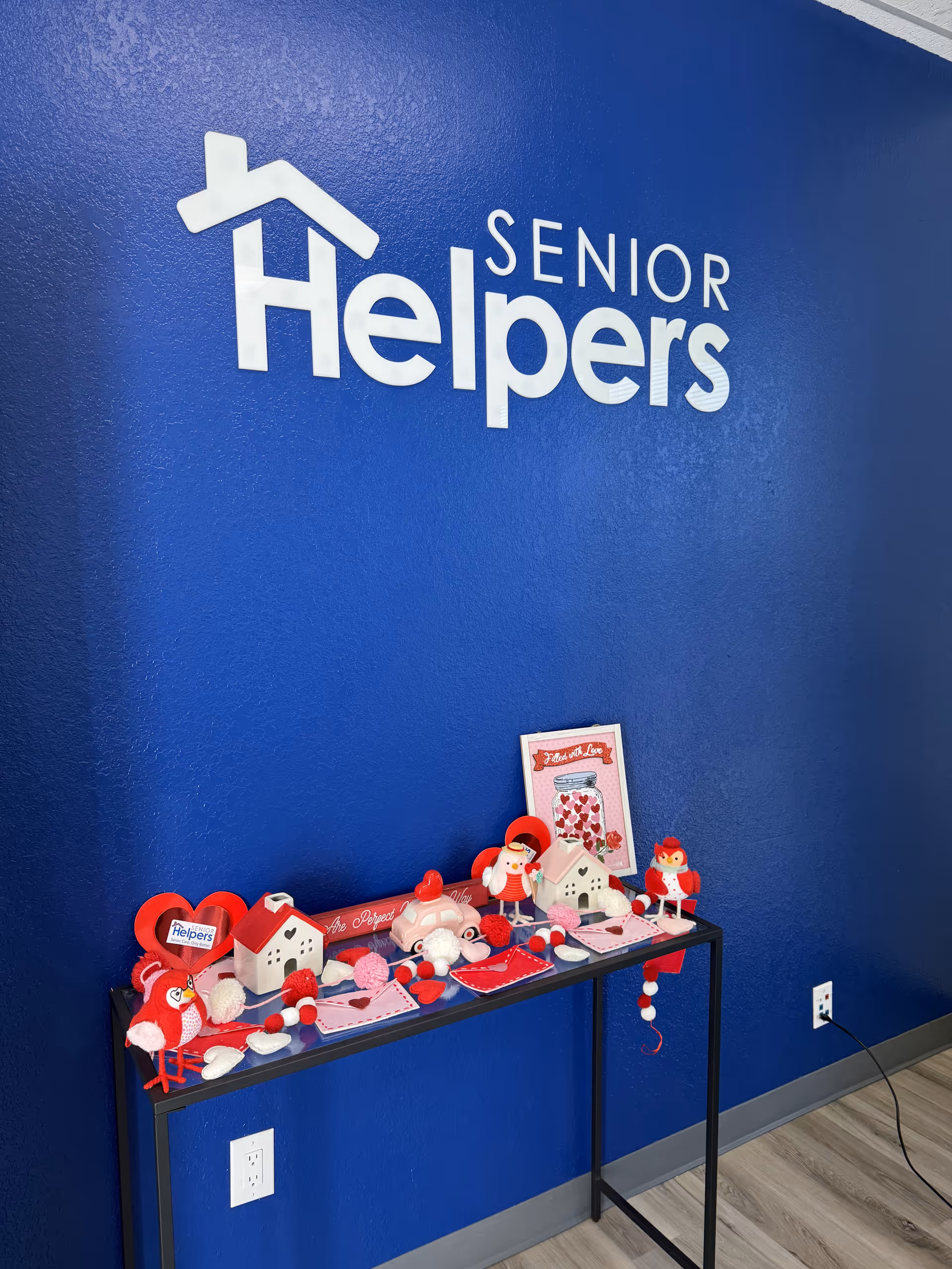 Blue interior wall with Senior Helpers logo and Valentine decorations on a table