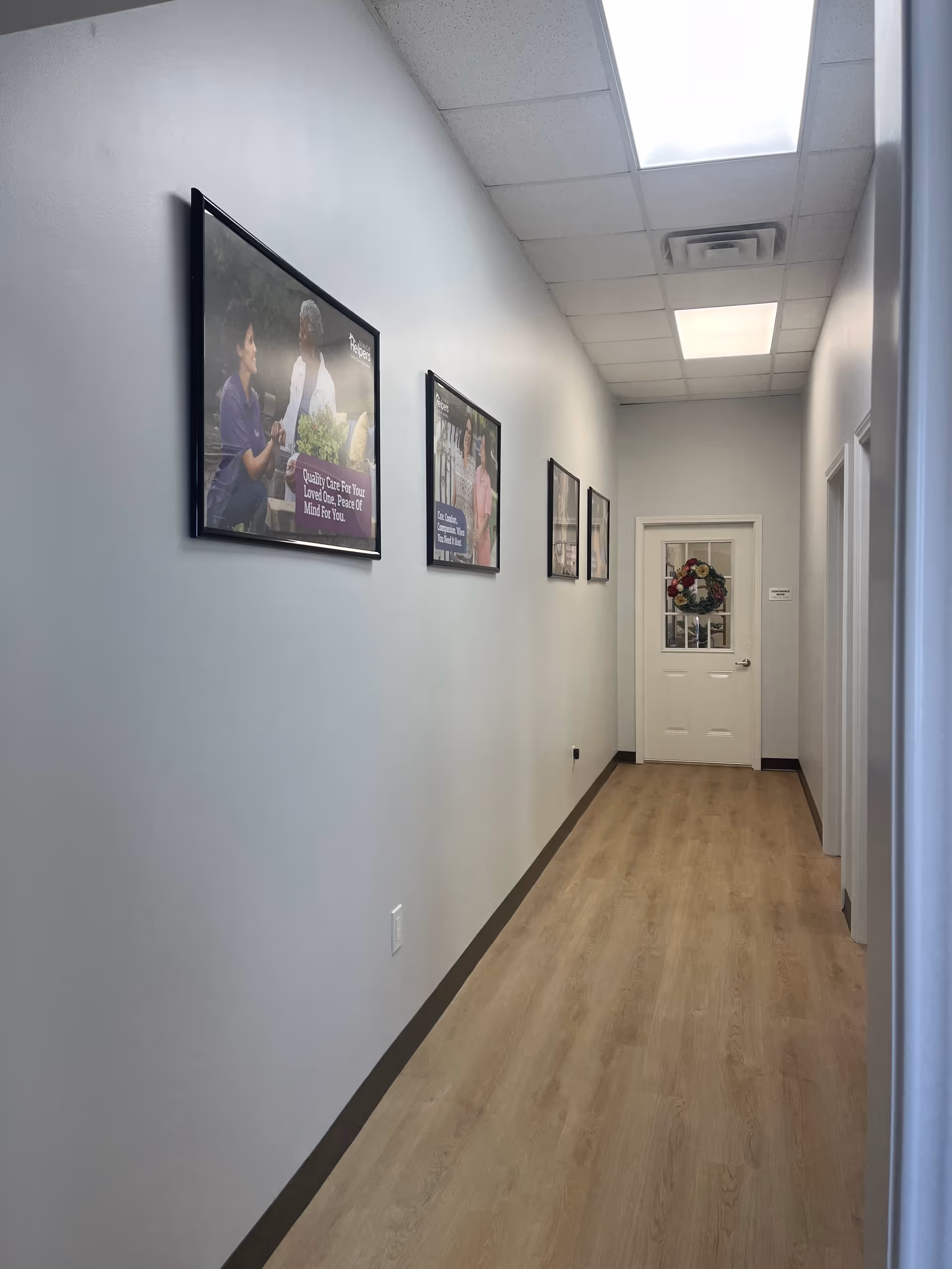 Long, well-lit hallway with framed pictures along pale walls and a decorated door at the end.