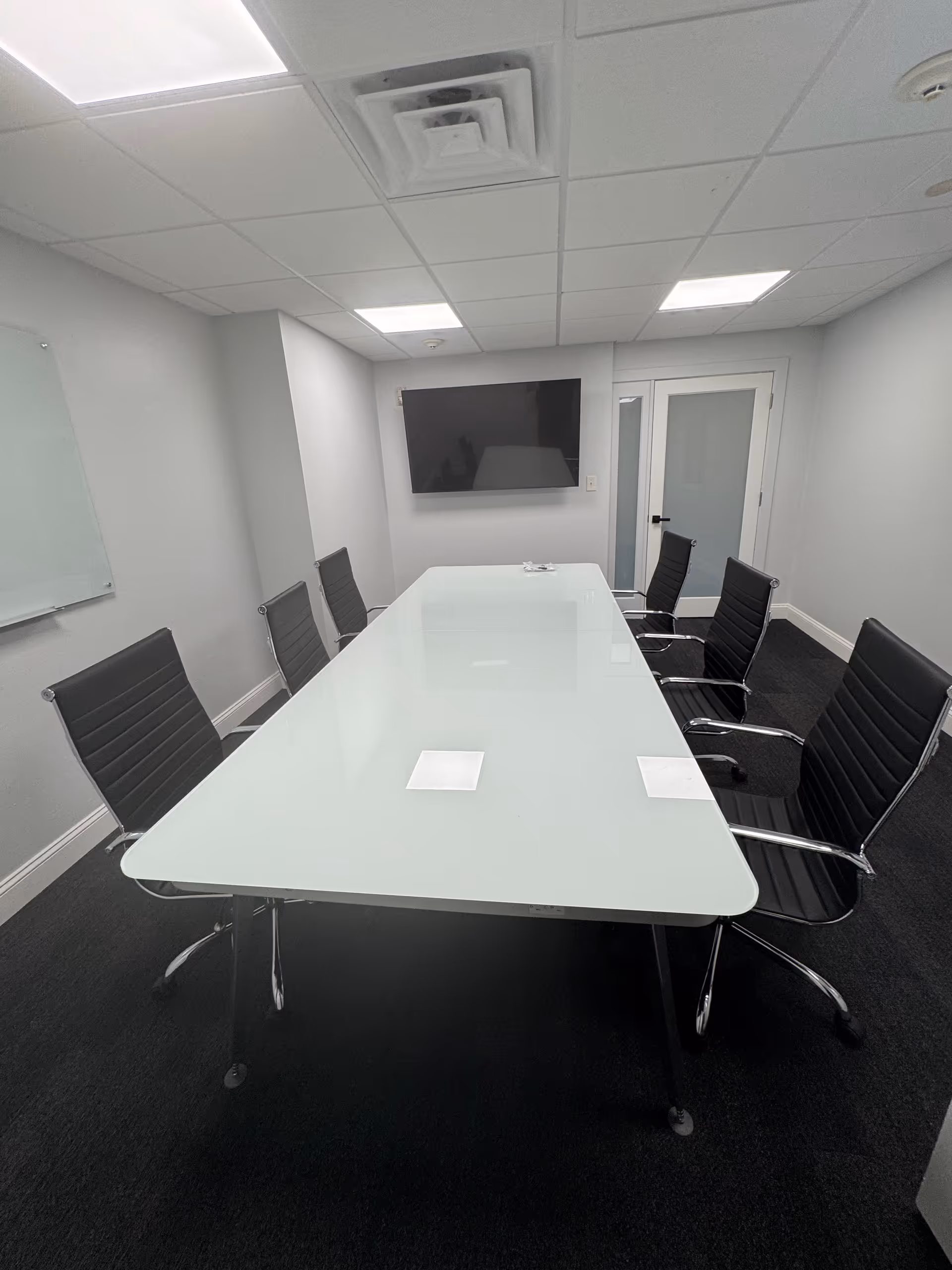 Modern conference room with a glass table and black chairs.