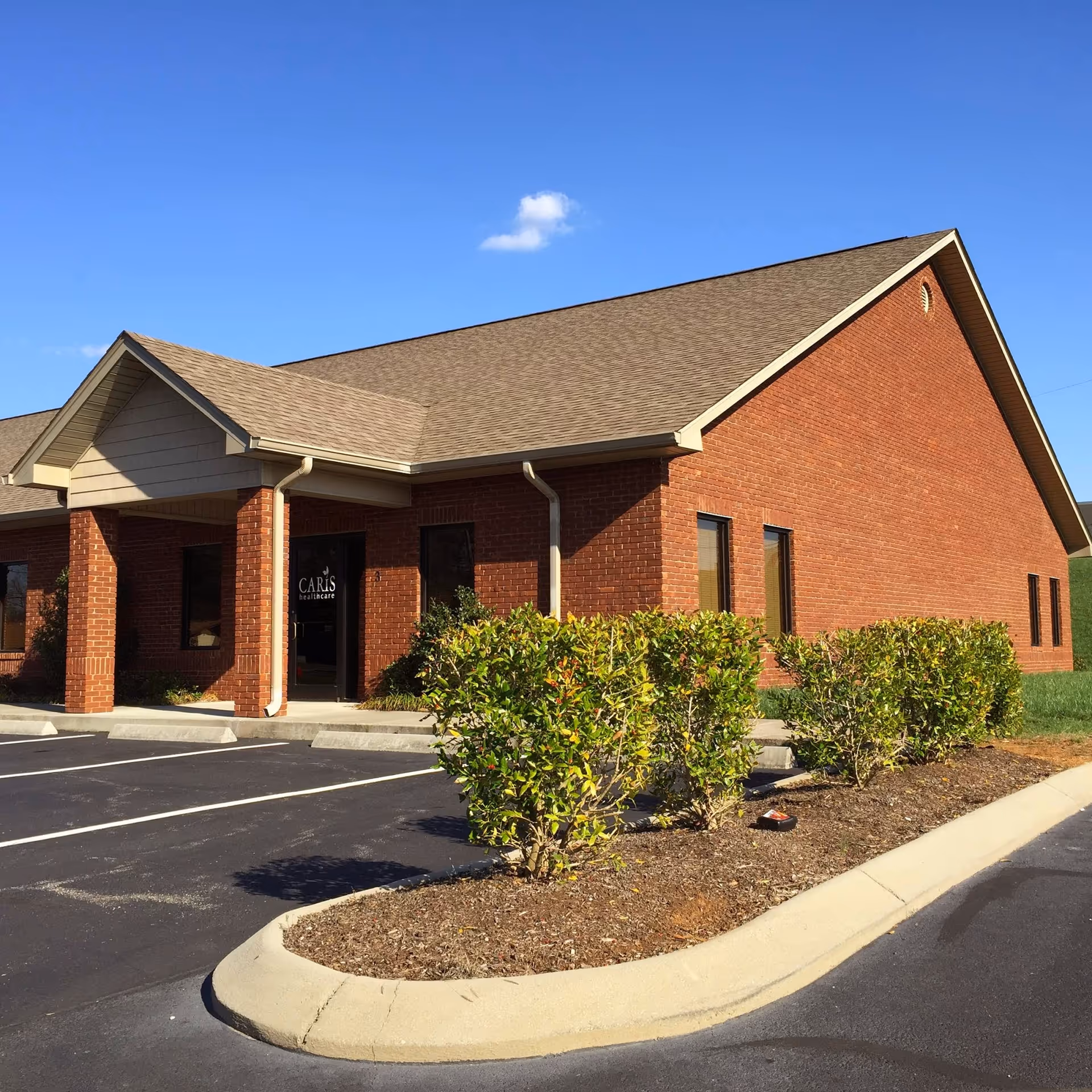 Exterior brick building of Caris Healthcare with parking lot and trimmed bushes in foreground.