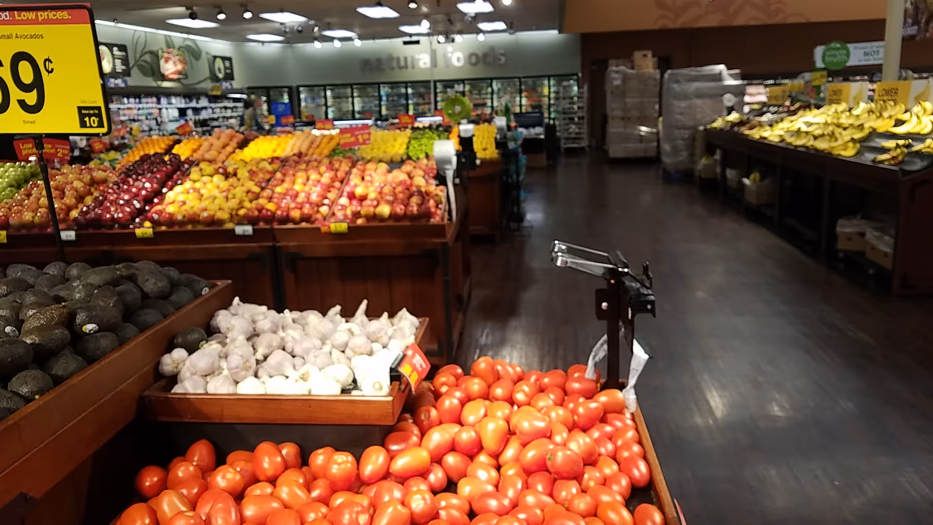 A grocery store produce section with apples, garlic, and tomatoes displayed in wooden crates.