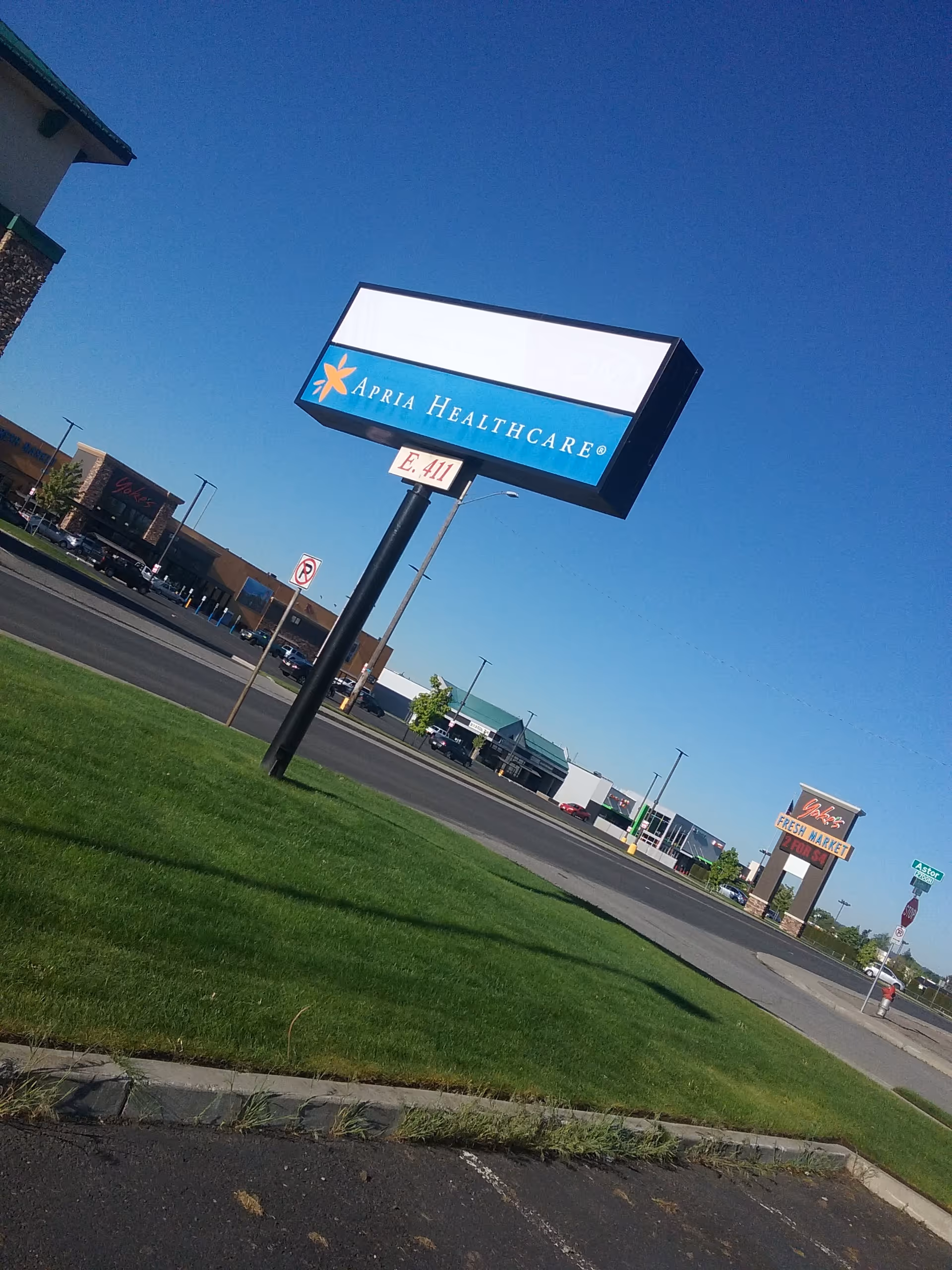 Apria Healthcare sign on a tall pole beside a grassy lot under blue sky.