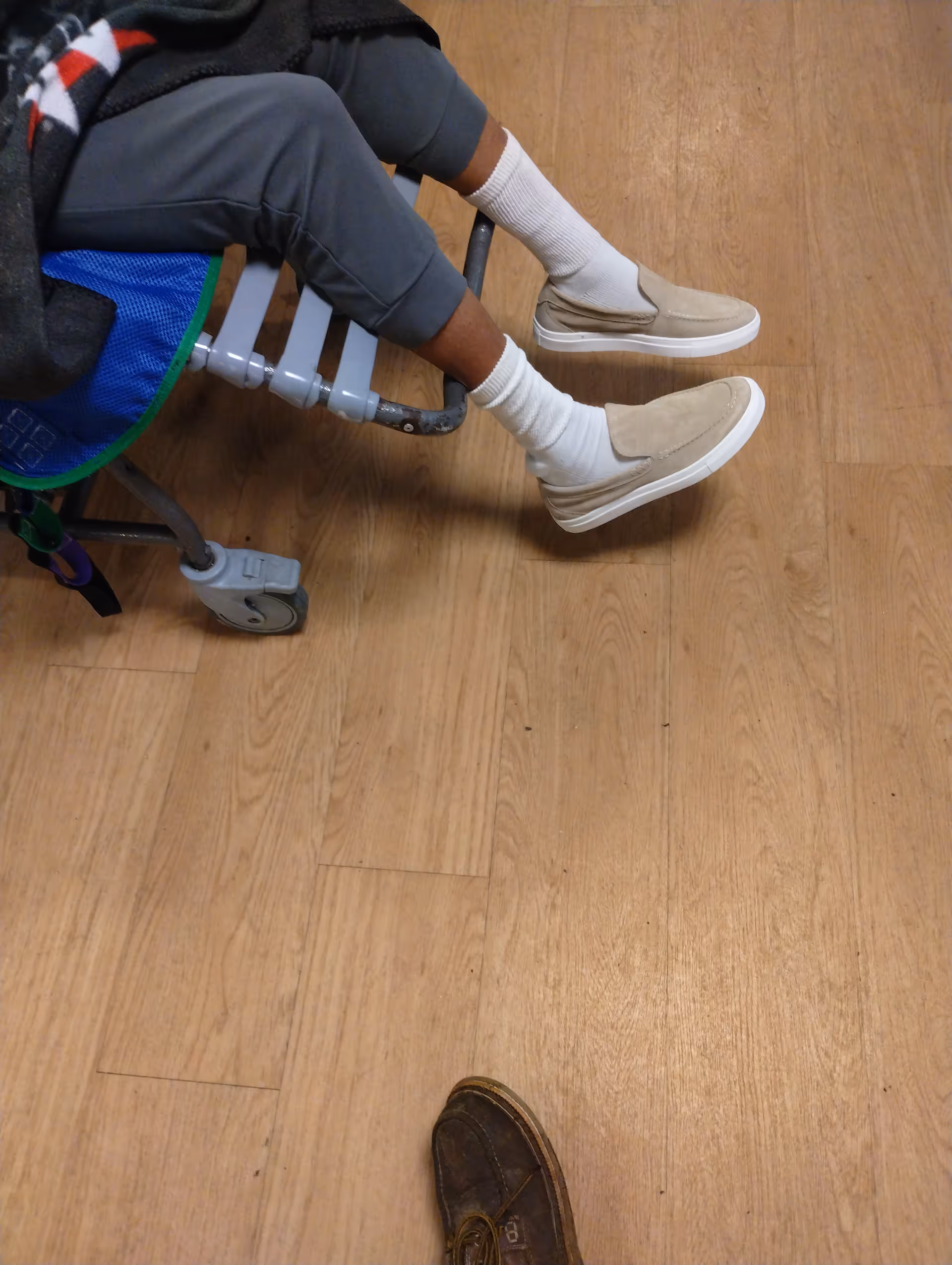 A person sits in a wheelchair on a wooden indoor floor.