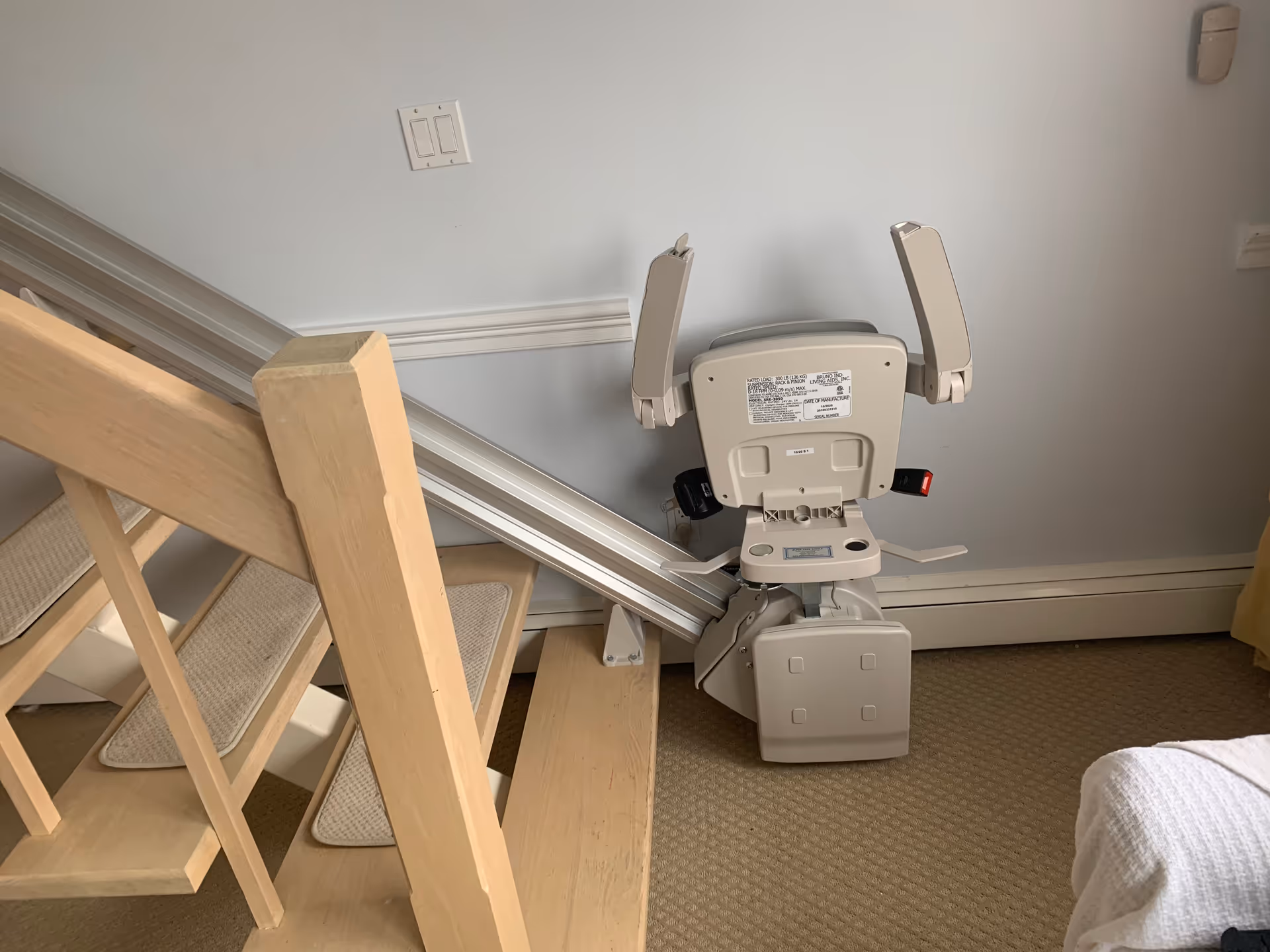 An indoor stair lift chair mounted along a wooden staircase in a residential facility.