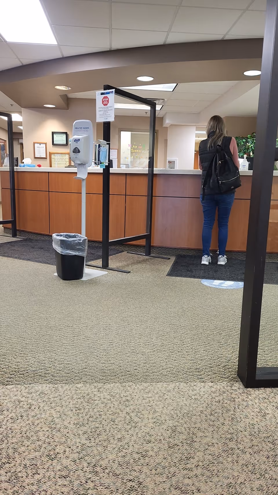 A person with backpack stands at a reception desk in a hospital lobby.