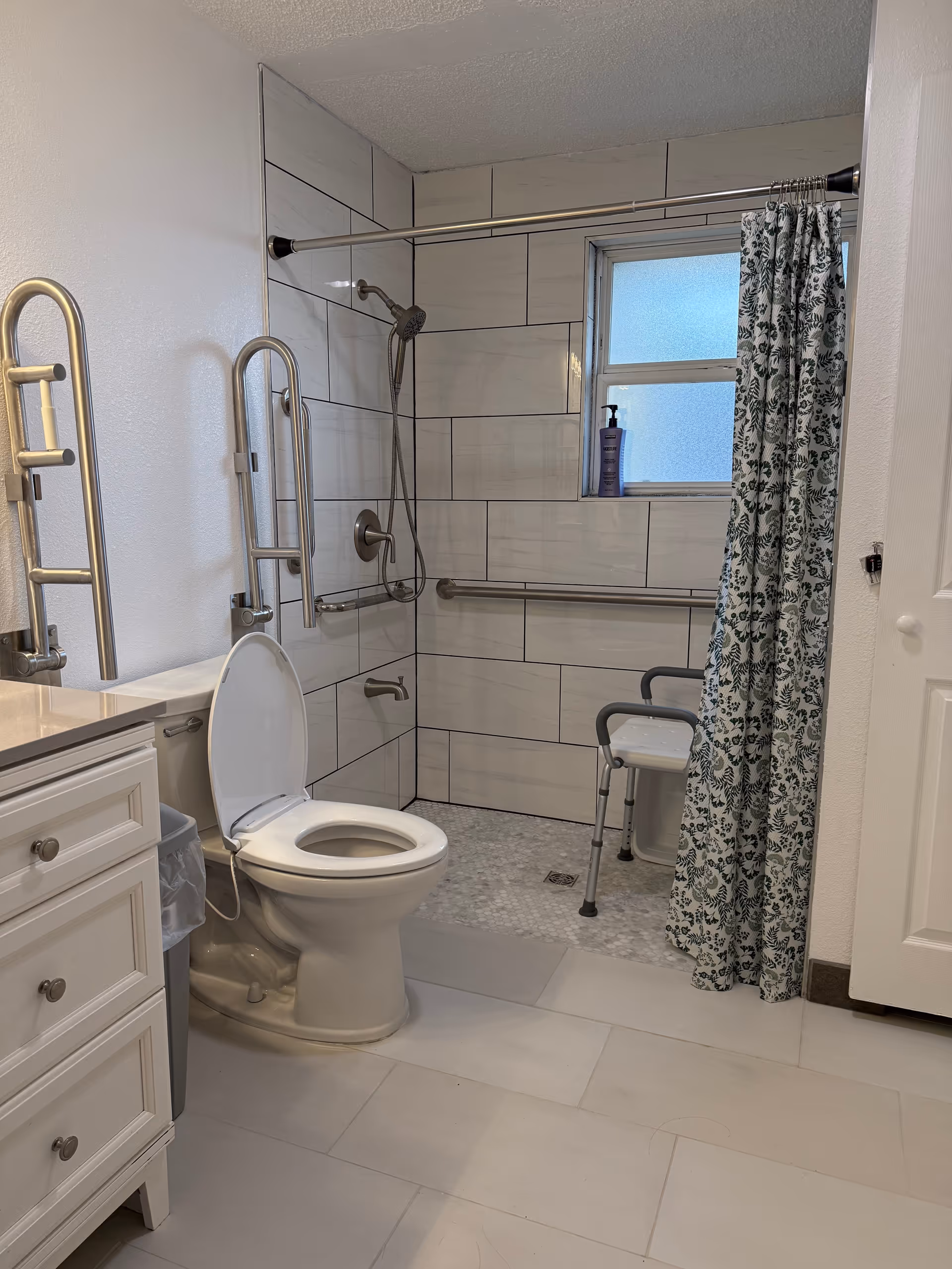 Accessible bathroom with toilet, shower, grab bars, curtain, and vanity.