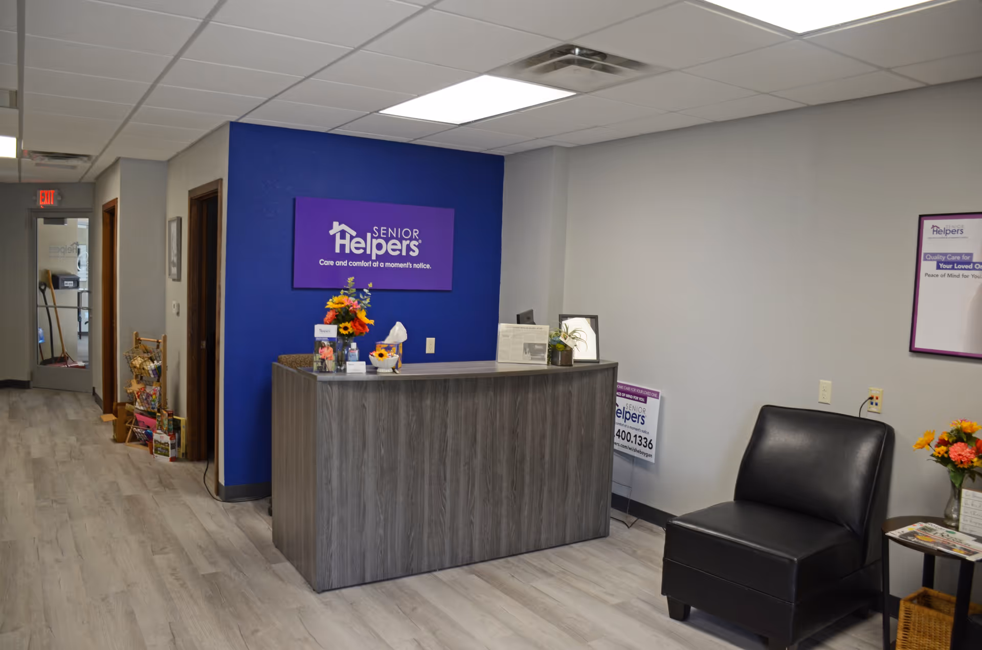 Reception area featuring a wood front desk, blue wall with Senior Helpers sign, and seating.