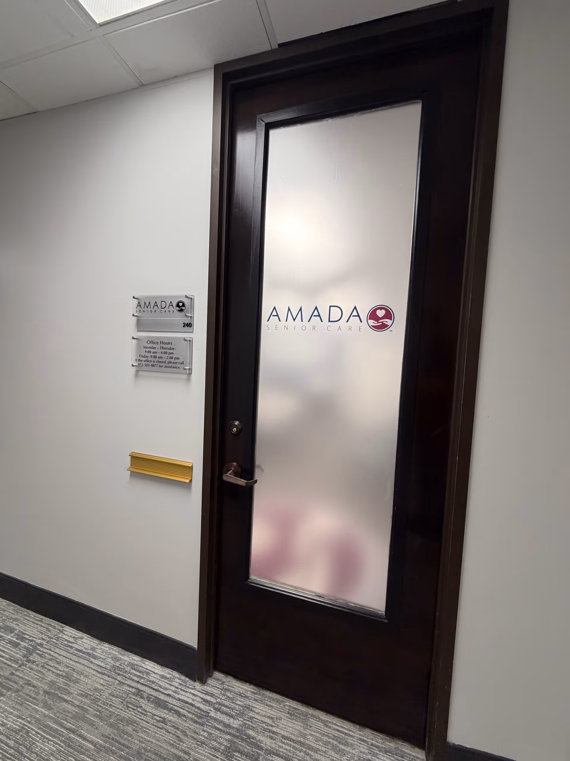 Interior hallway with a frosted glass door labeled Amada Senior Care and wall plaque.