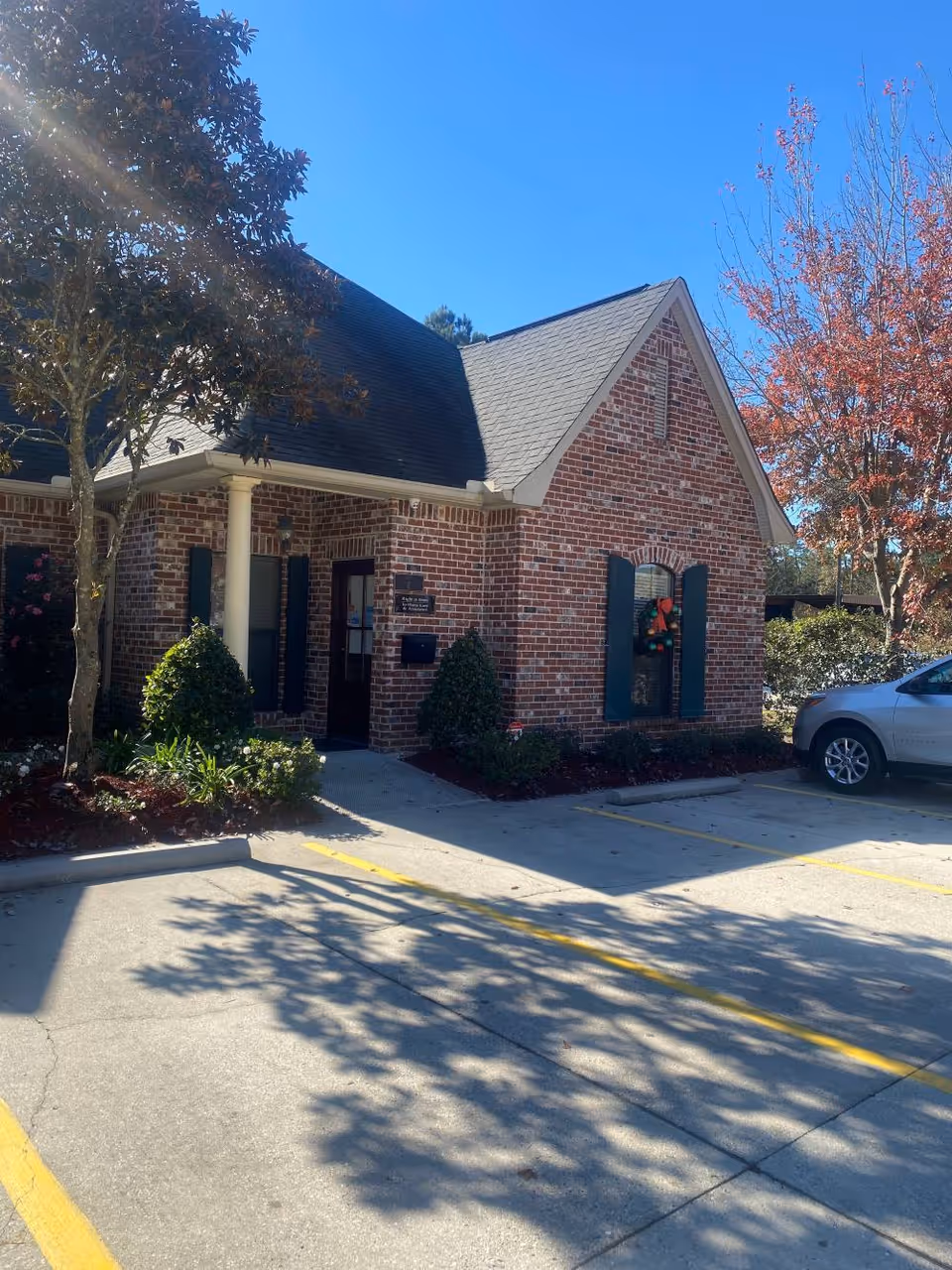 Brick senior living facility with an entrance, shutters, shrubs, and a car in the parking lot.
