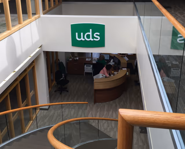 Inside a building lobby, a curved wooden reception desk with staff at work under uds sign.