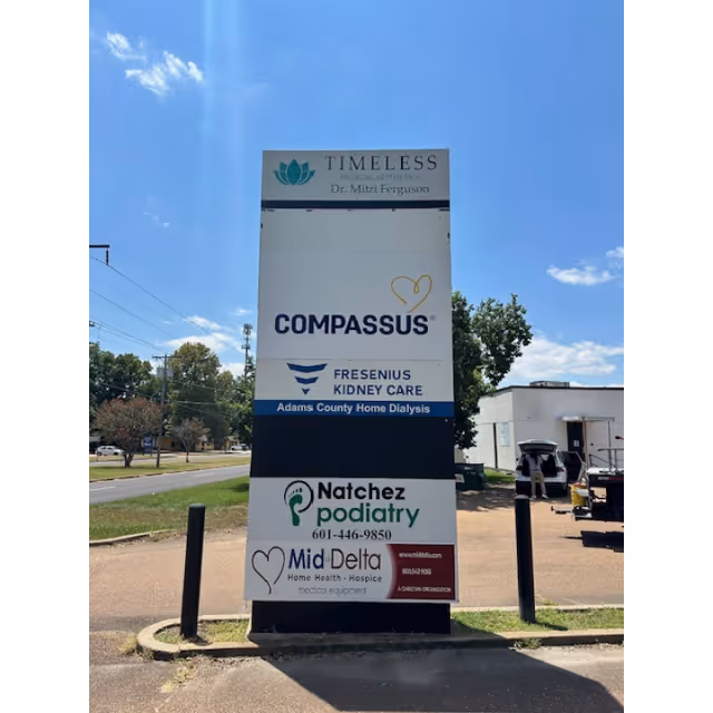 Tall outdoor signboard displaying Compassus and other healthcare providers against a blue sky.