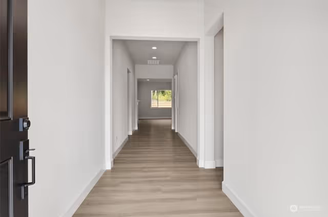 Bright empty hallway with white walls and light wood flooring in a residential facility.