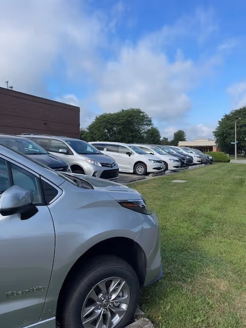 Row of parked cars along a grassy area in front of a brick building