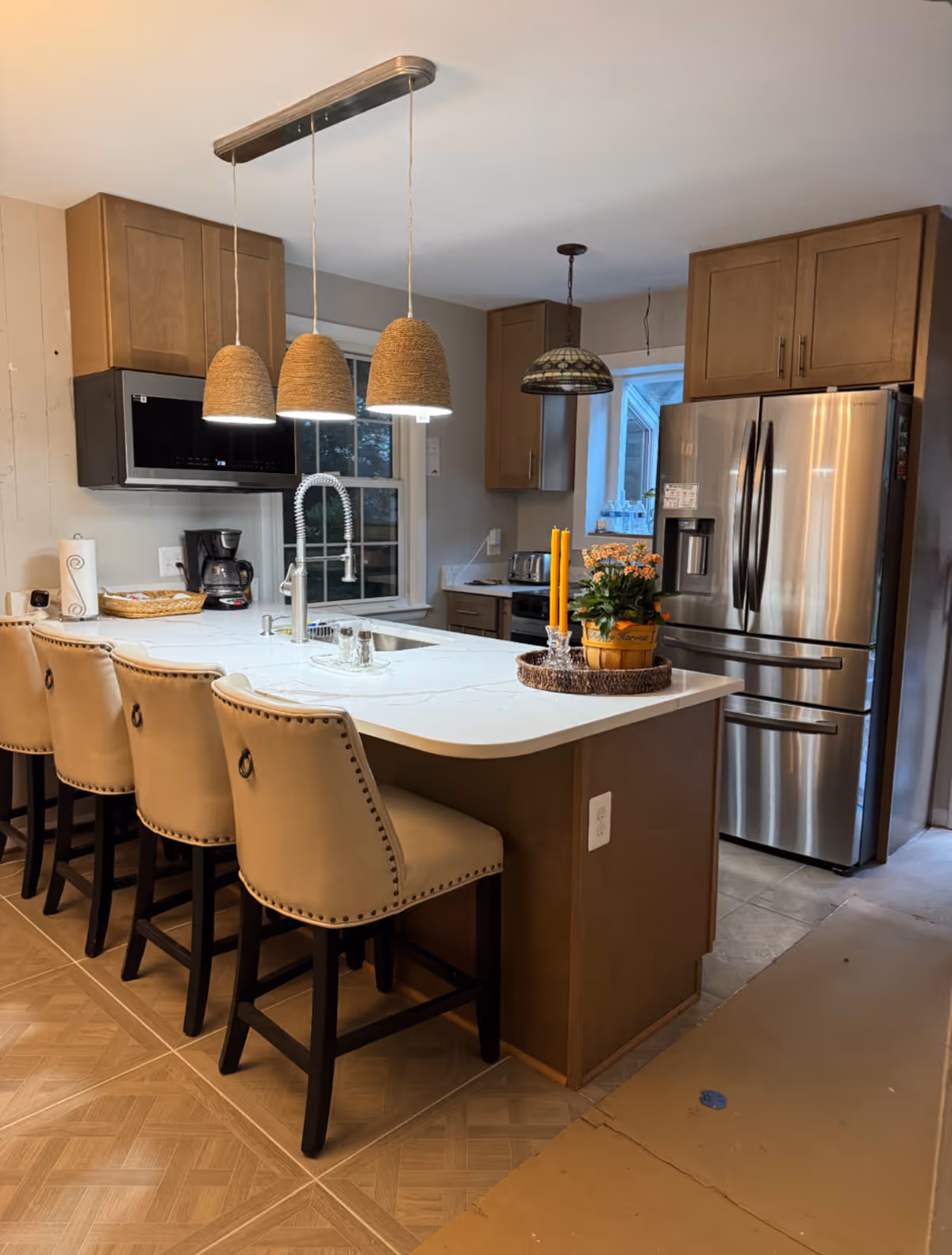 Modern kitchen with island, pendant lights, stainless steel fridge, and bar stools.