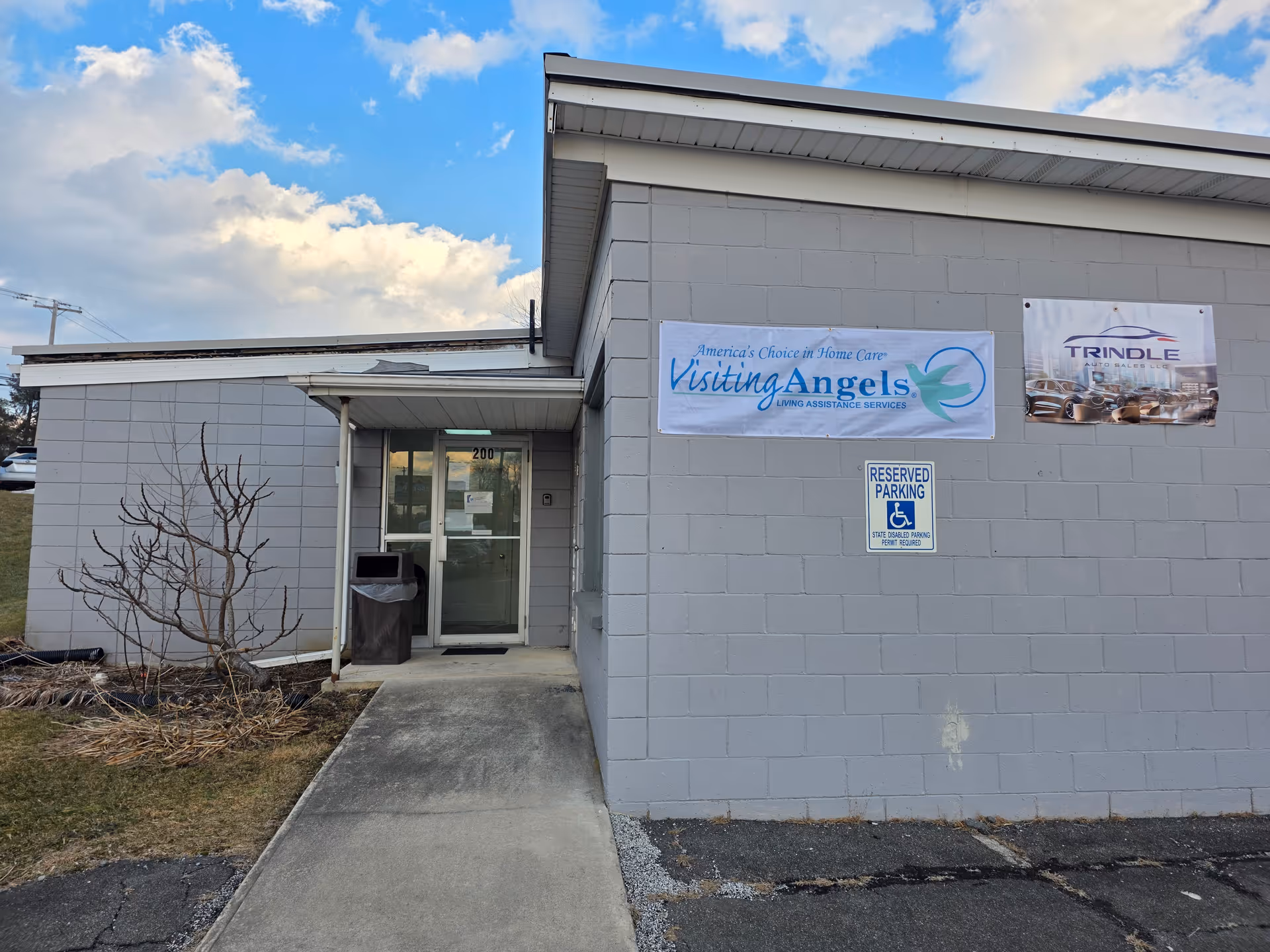 Grey exterior building with glass door entrance and banners advertising Visiting Angels.