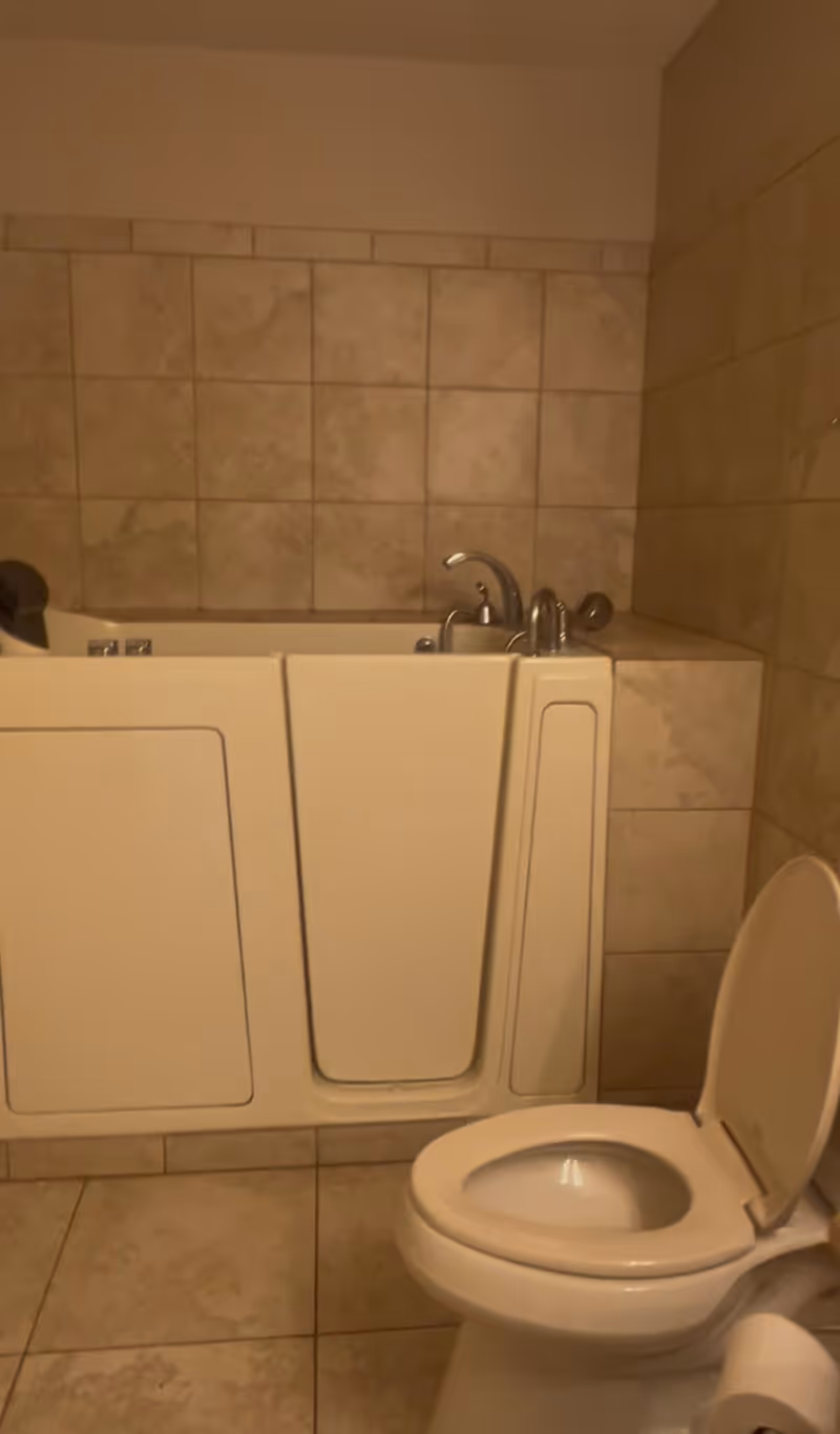 Accessible walk-in bathtub and toilet in a tiled senior living facility bathroom.