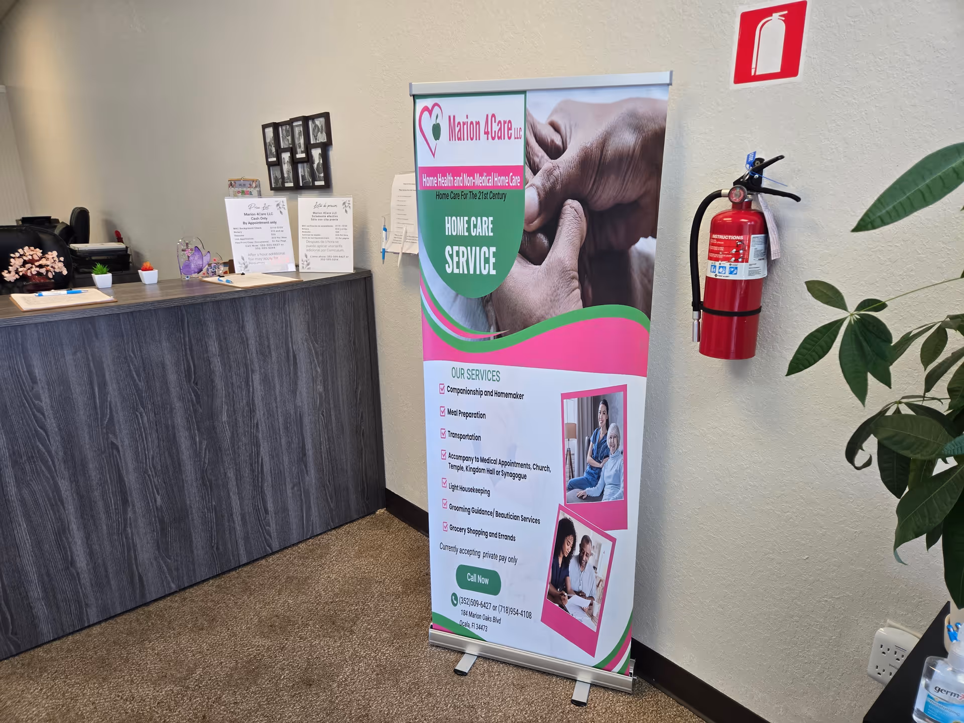 Indoor reception area with a tall Marion 4Care banner, desk, fire extinguisher, and plant.