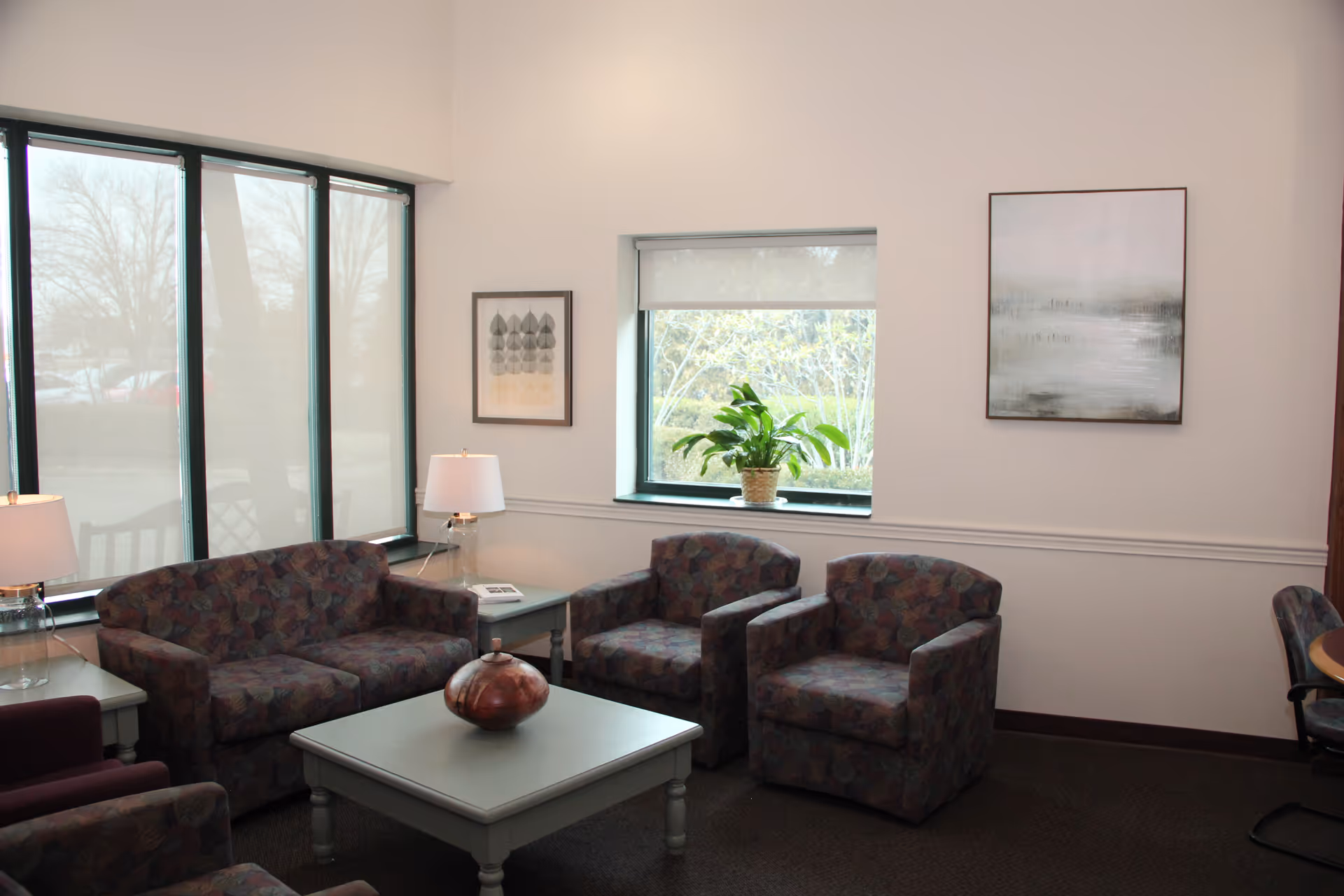 Cozy lounge with patterned chairs, a coffee table, lamps, and large windows.