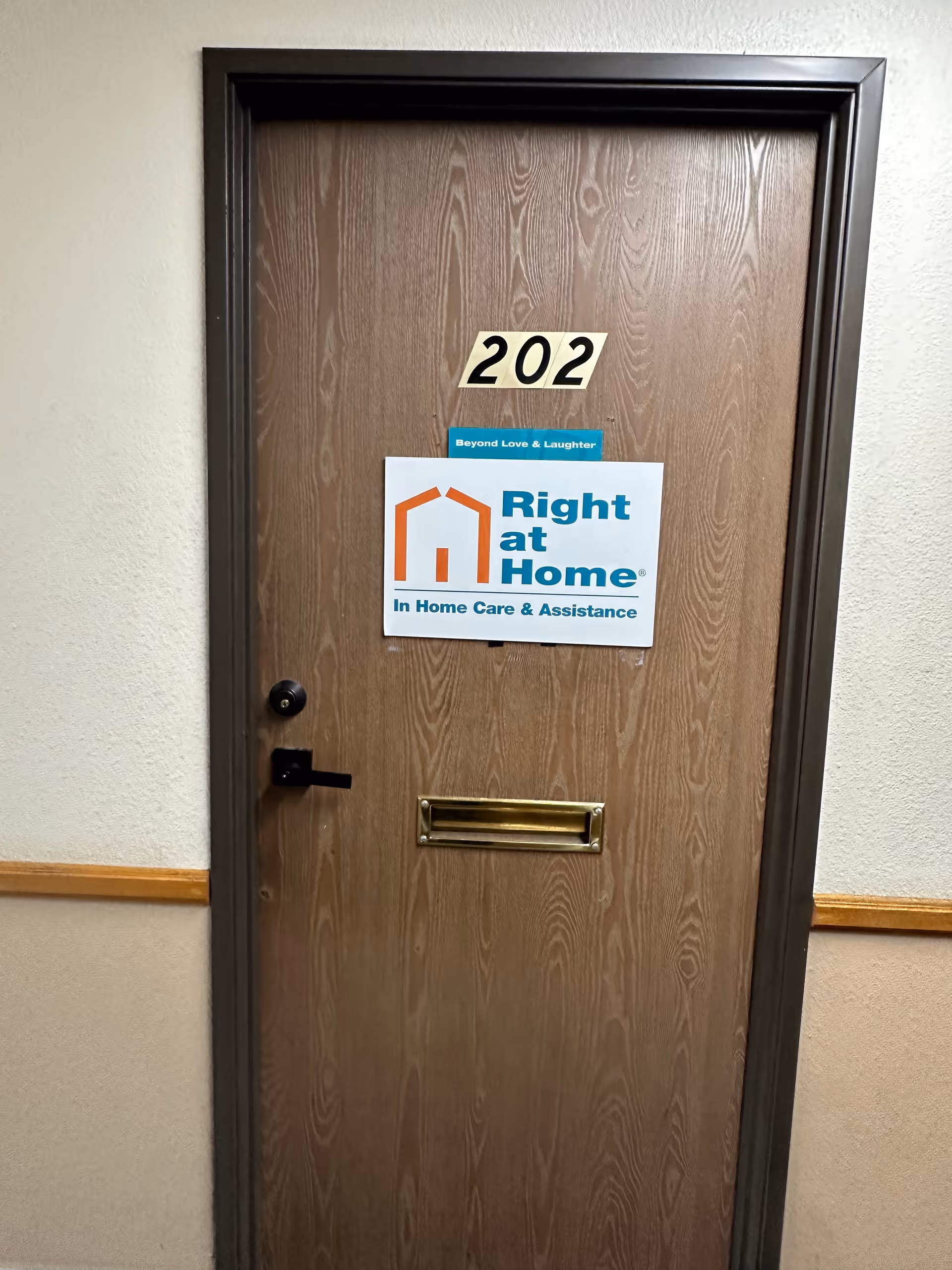 Interior wooden hallway door labeled 202 with a Right at Home sign.