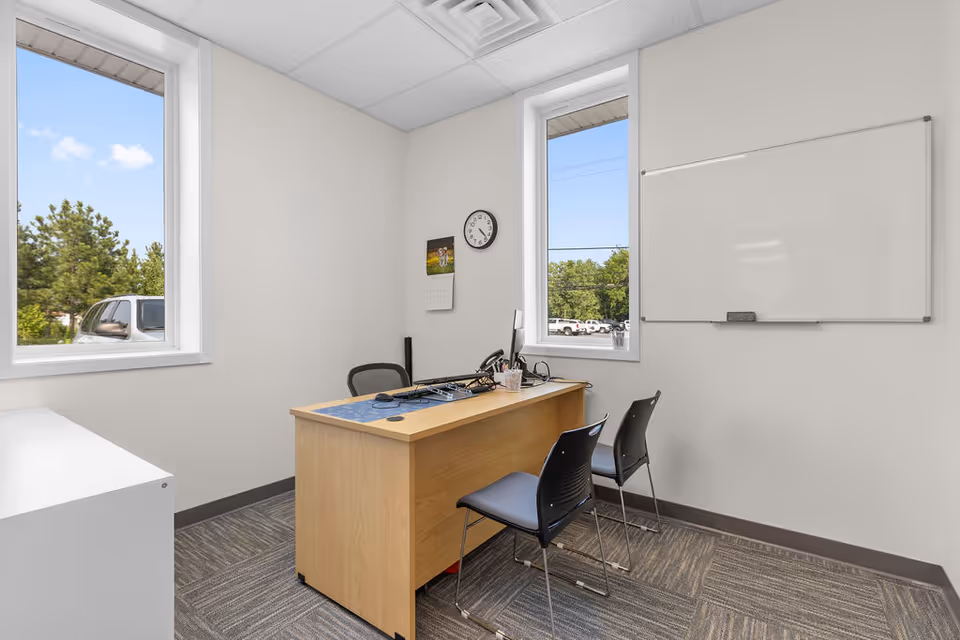 An empty office in a senior living facility with a desk, chairs, and whiteboard.