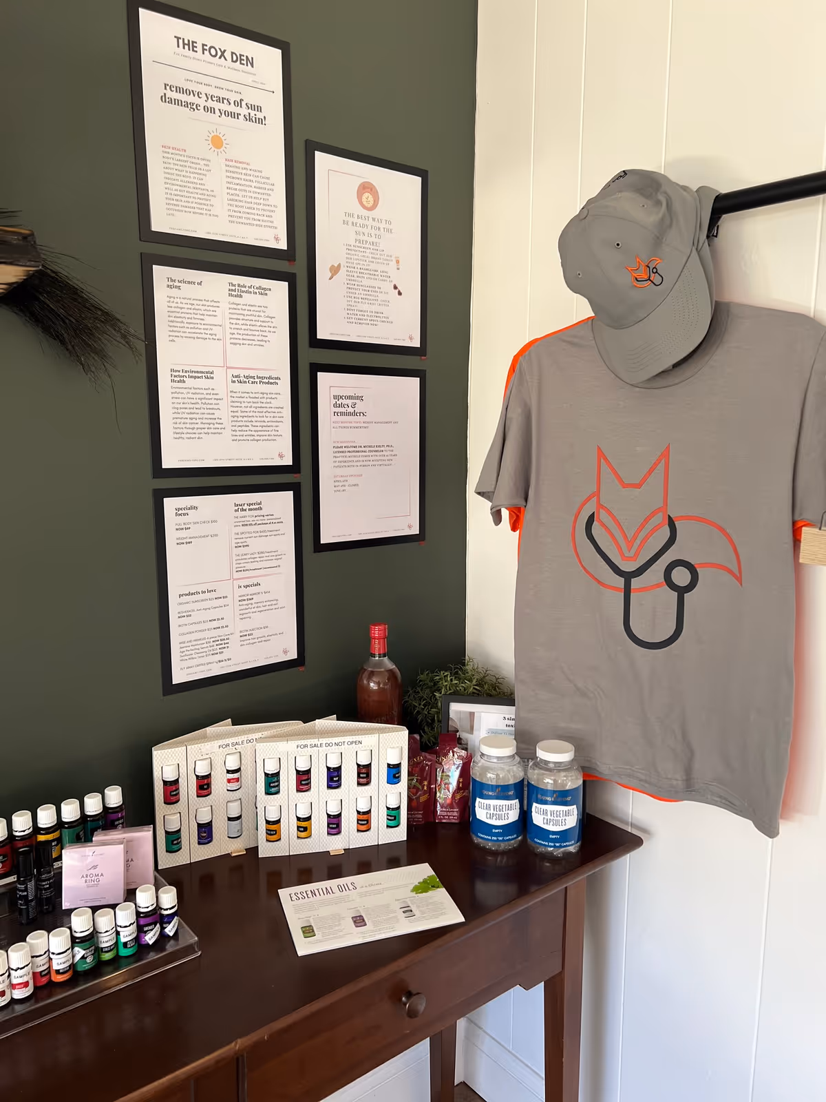 Interior corner with framed posters, a hanging shirt and hat, and a desk of essential oils.