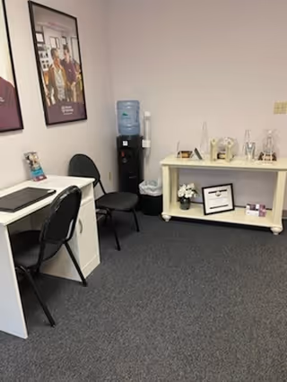 Small interior room with a desk, chairs, water cooler, and a decorative shelf.