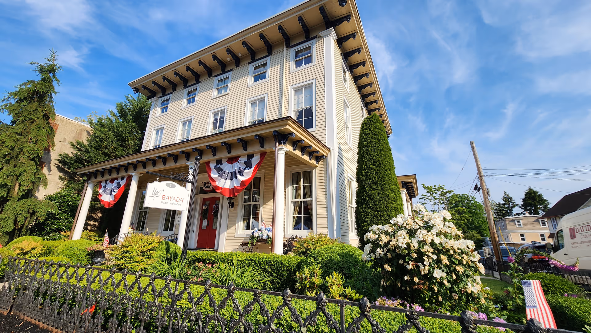 Three-story beige building labeled BAYADA Pediatrics with patriotic bunting and manicured garden.
