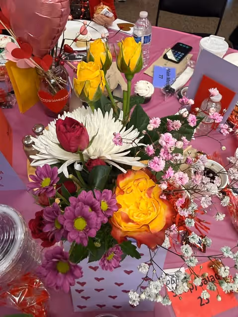 Colorful flower arrangement on a pink table with decor and cards.