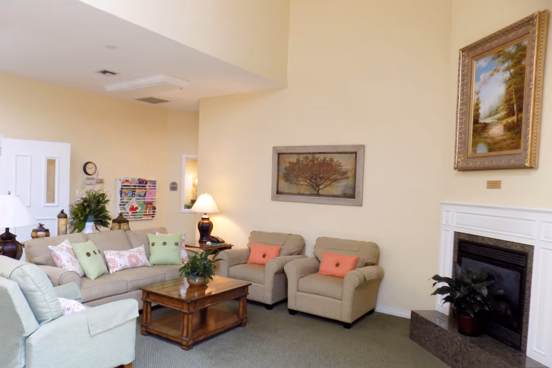 Cozy living room lounge with beige seating, coffee table, plants, and fireplace.