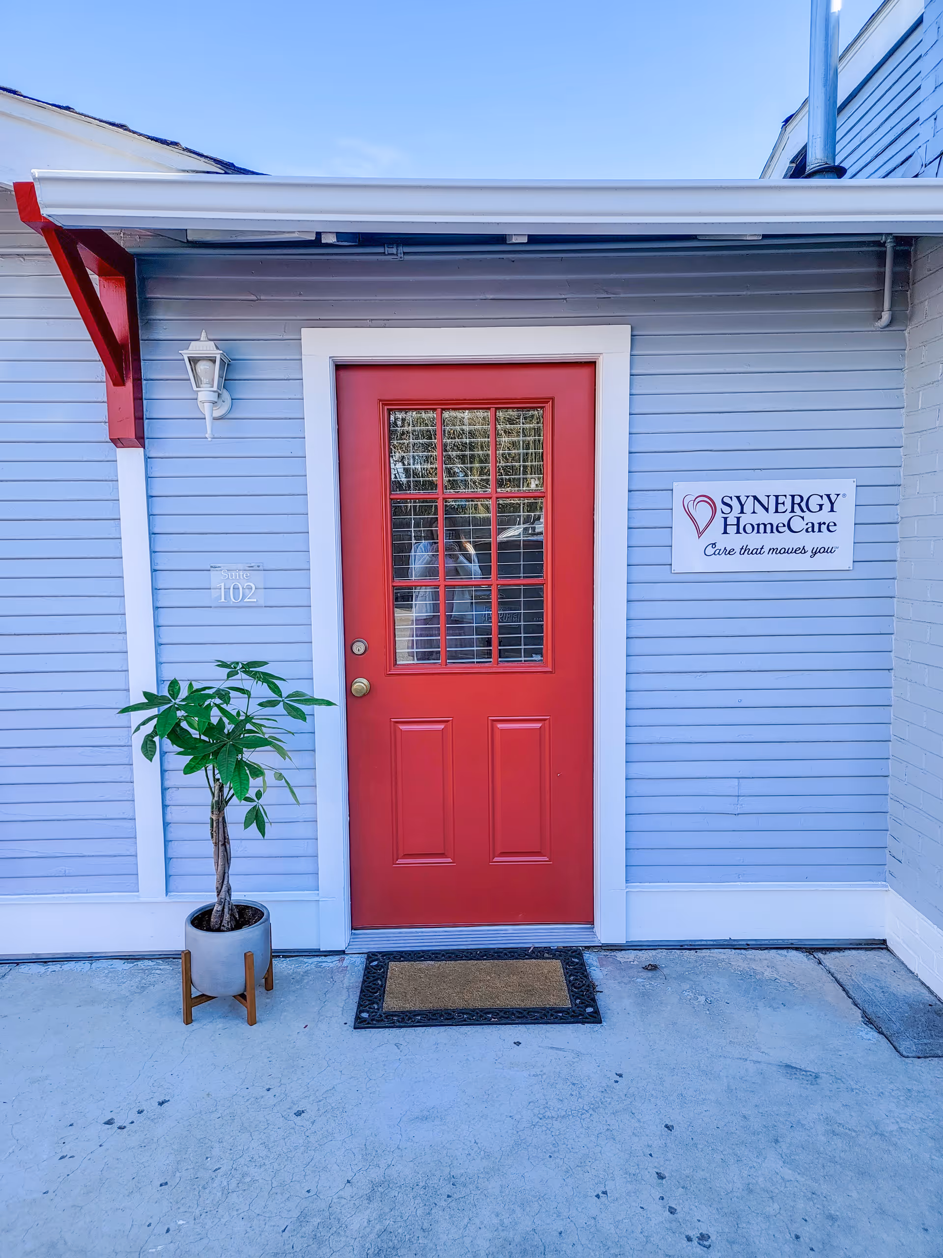 Exterior of a Synergy HomeCare facility with a red front door and potted plant.