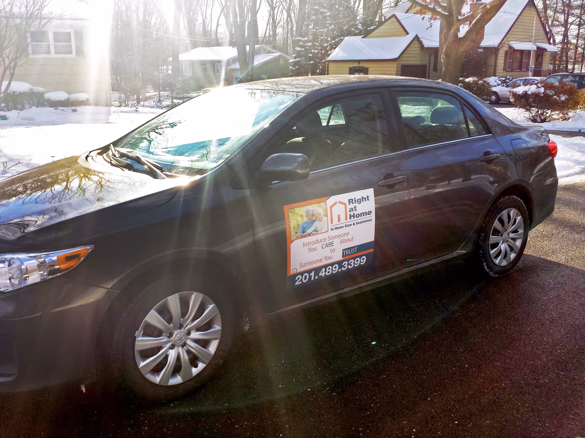 Black sedan with Right at Home sign parked on a snowy residential street