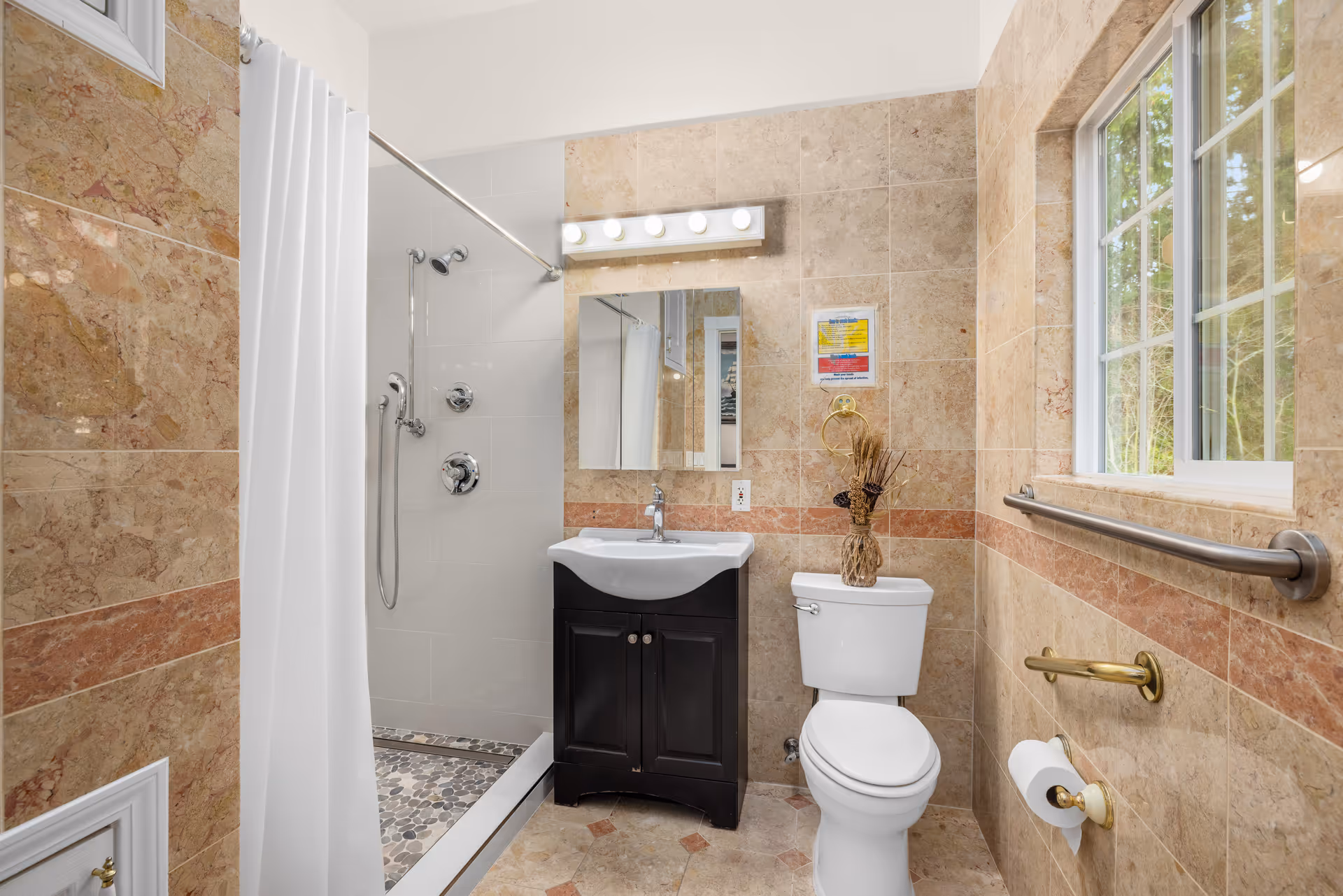 Bathroom with shower, sink, toilet, and window in tiled room.