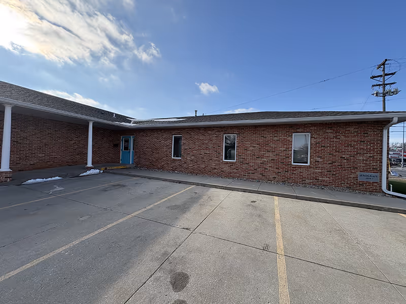 Brick, single-story building exterior with a blue front door and parking lot.