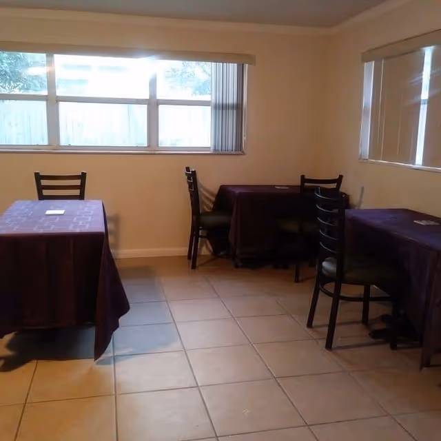 A small dining area with purple tablecloths and wooden chairs by windows.