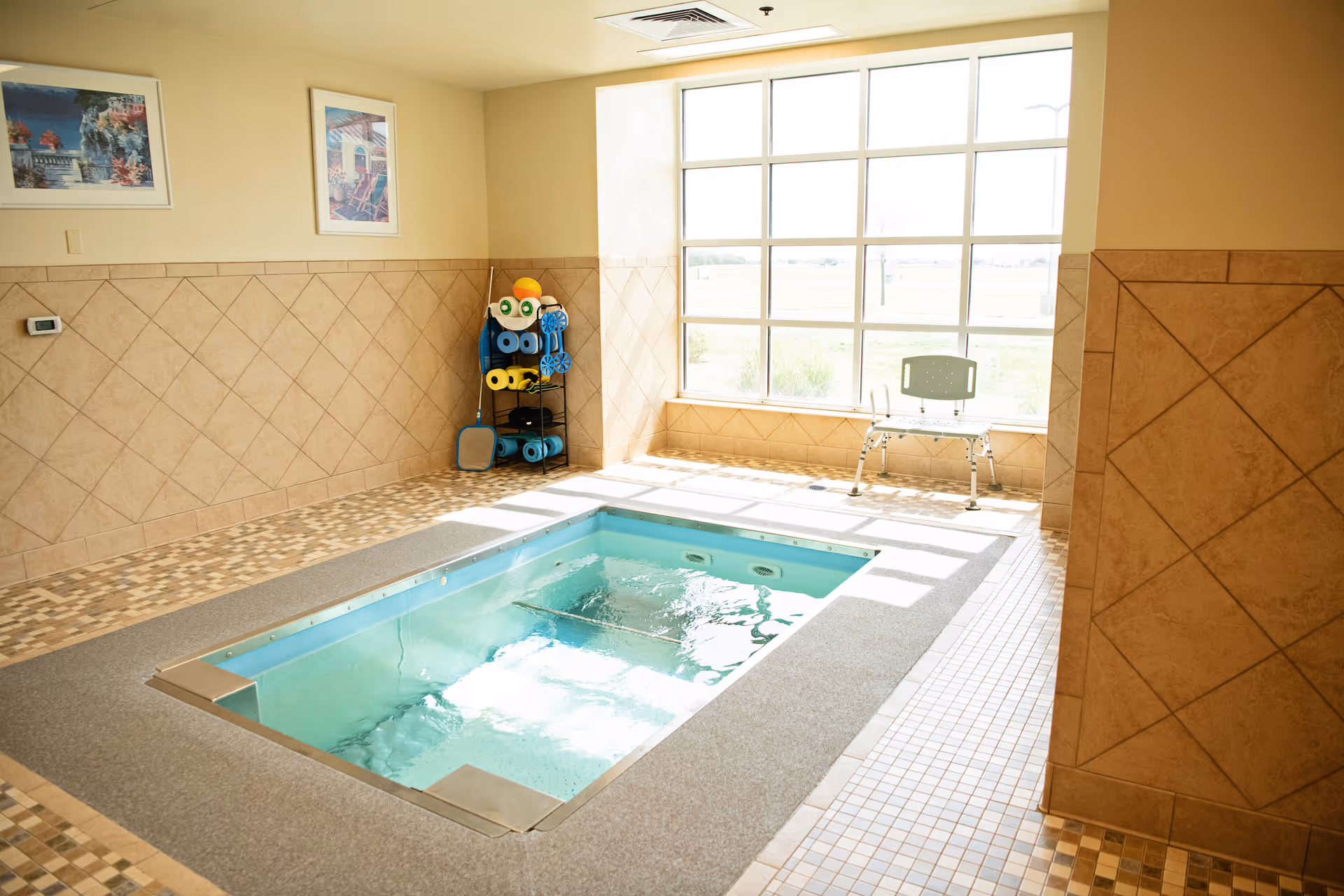 Indoor pool area with tiled walls, large window, towel rack, and seating.