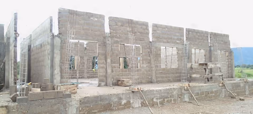 Unfinished concrete block building under construction with ladders and scaffolding outside.