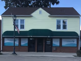 Two-story Visiting Angels storefront with green awning and American flag.