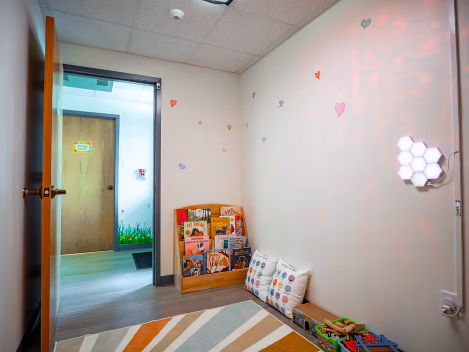 Bright playroom with books, pillows, and toys arranged along a wall in a welcoming space.