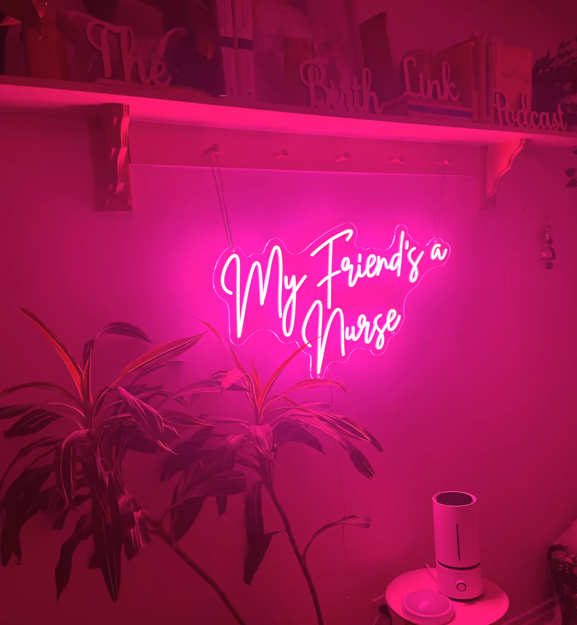 Interior with bright pink neon sign reading 'My Friend's a Nurse' beside a leafy plant.