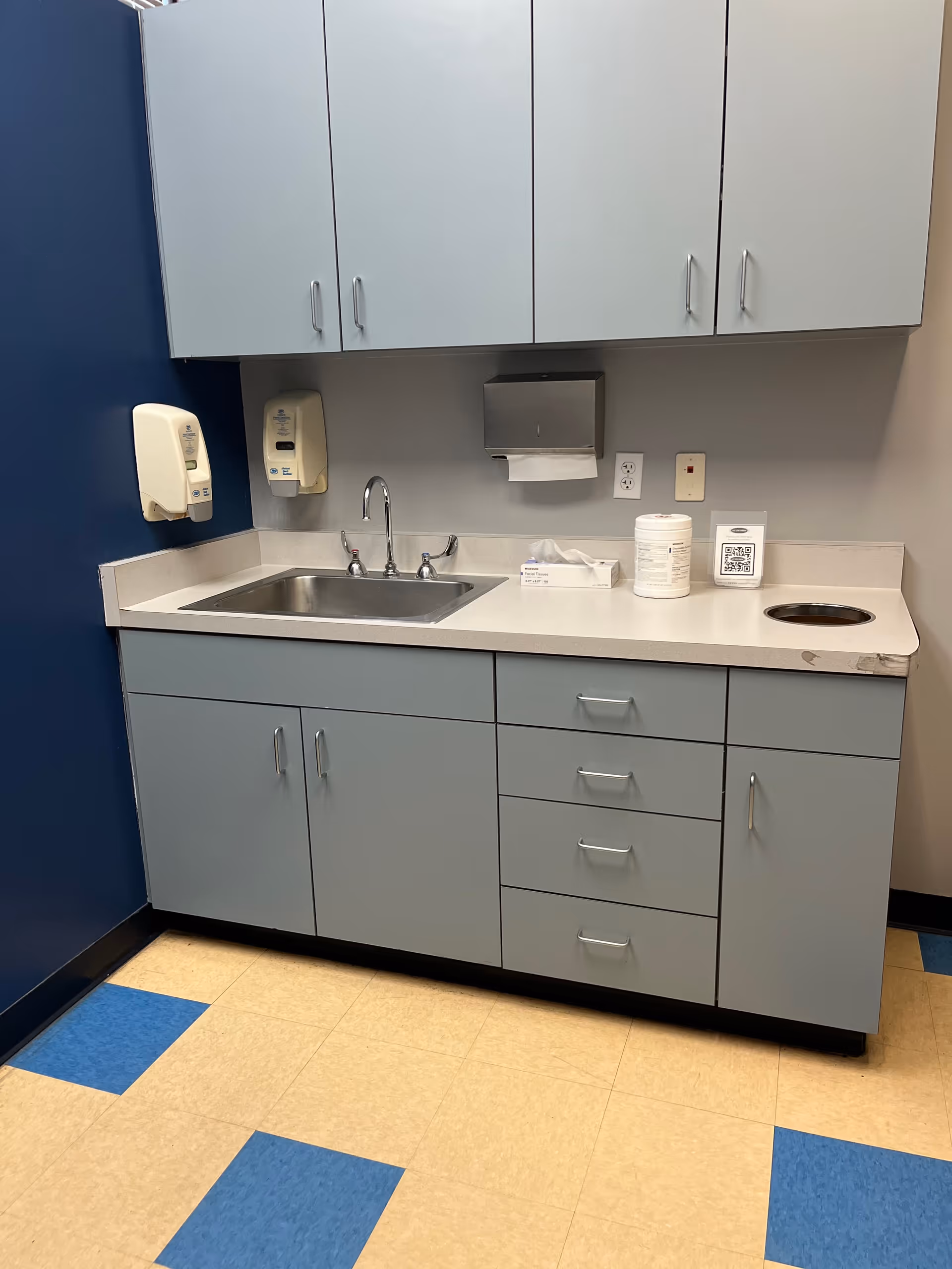 Blue-gray kitchen with sink, cabinets, and paper towel dispenser.