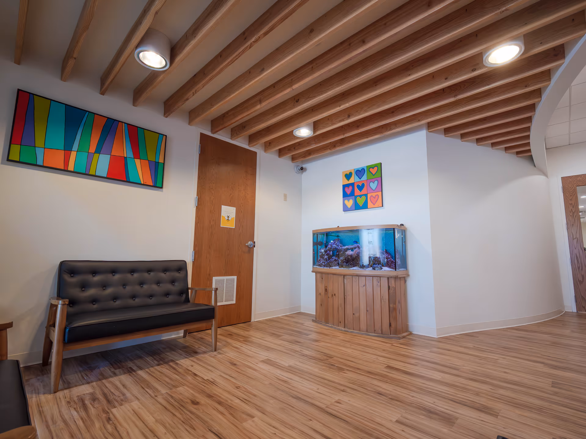 A welcoming lounge with a black tufted sofa, aquarium, wood floors, and colorful wall art.