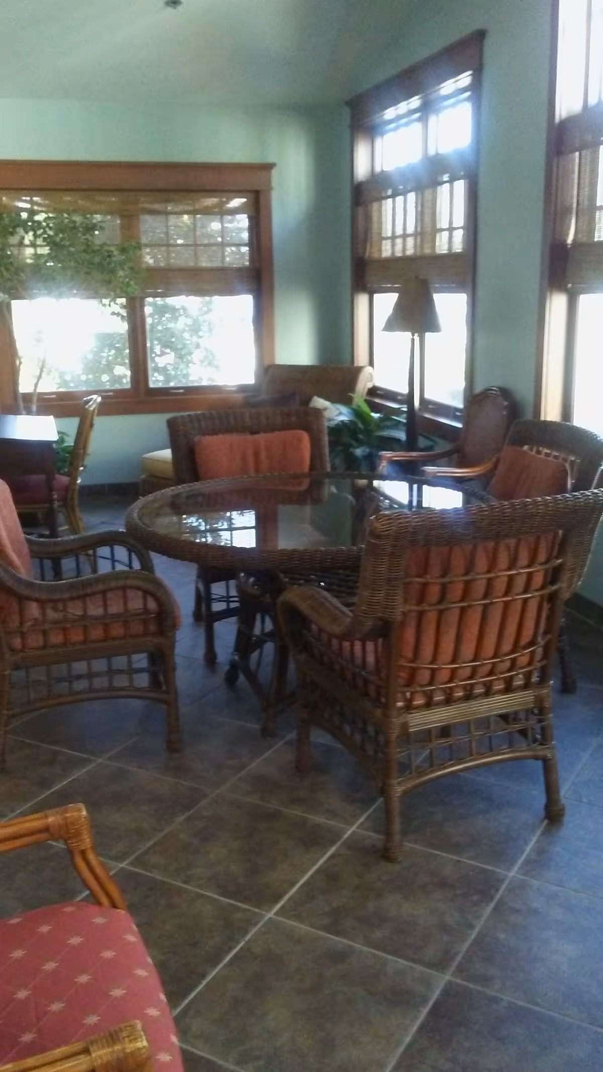 Cozy sunlit living room seating area with wicker chairs around a glass table.
