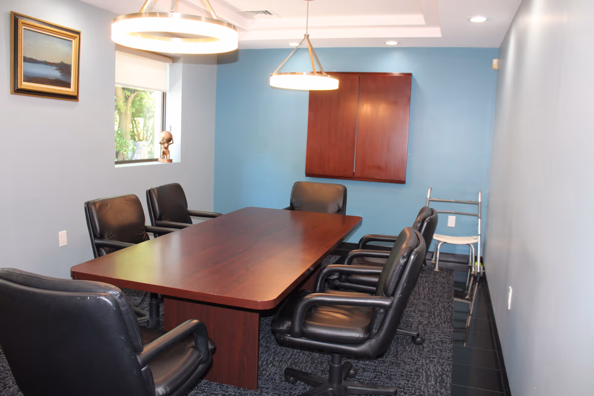 A conference room with a dark wood table and black leather chairs.