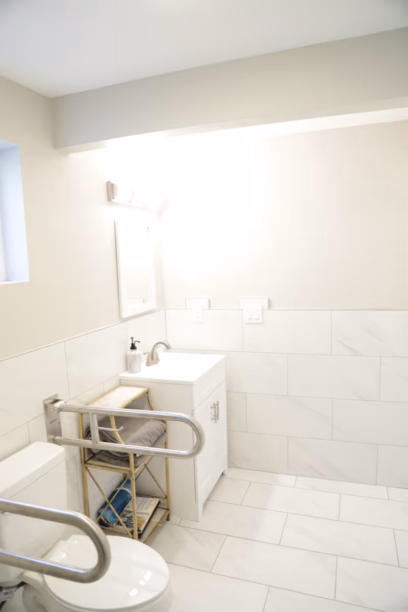 Accessible bathroom with white tiles, sink, mirror, and grab bars.