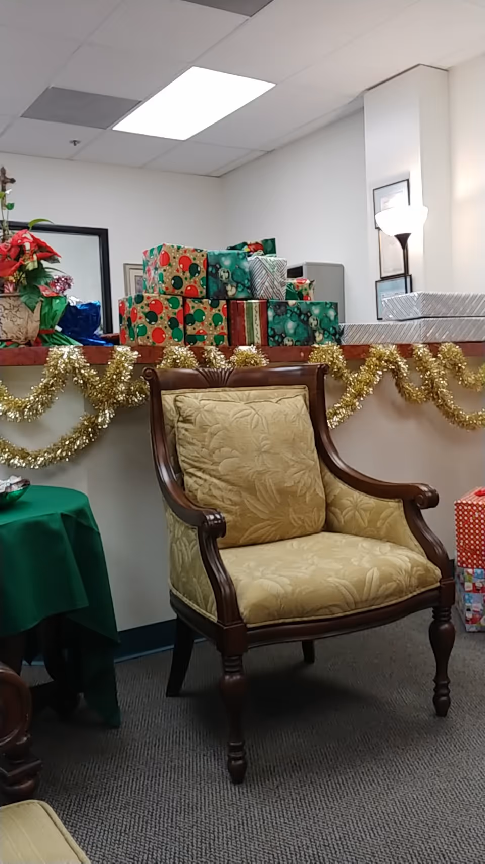 Ornate beige armchair beside a festive display of wrapped gifts and gold garland.