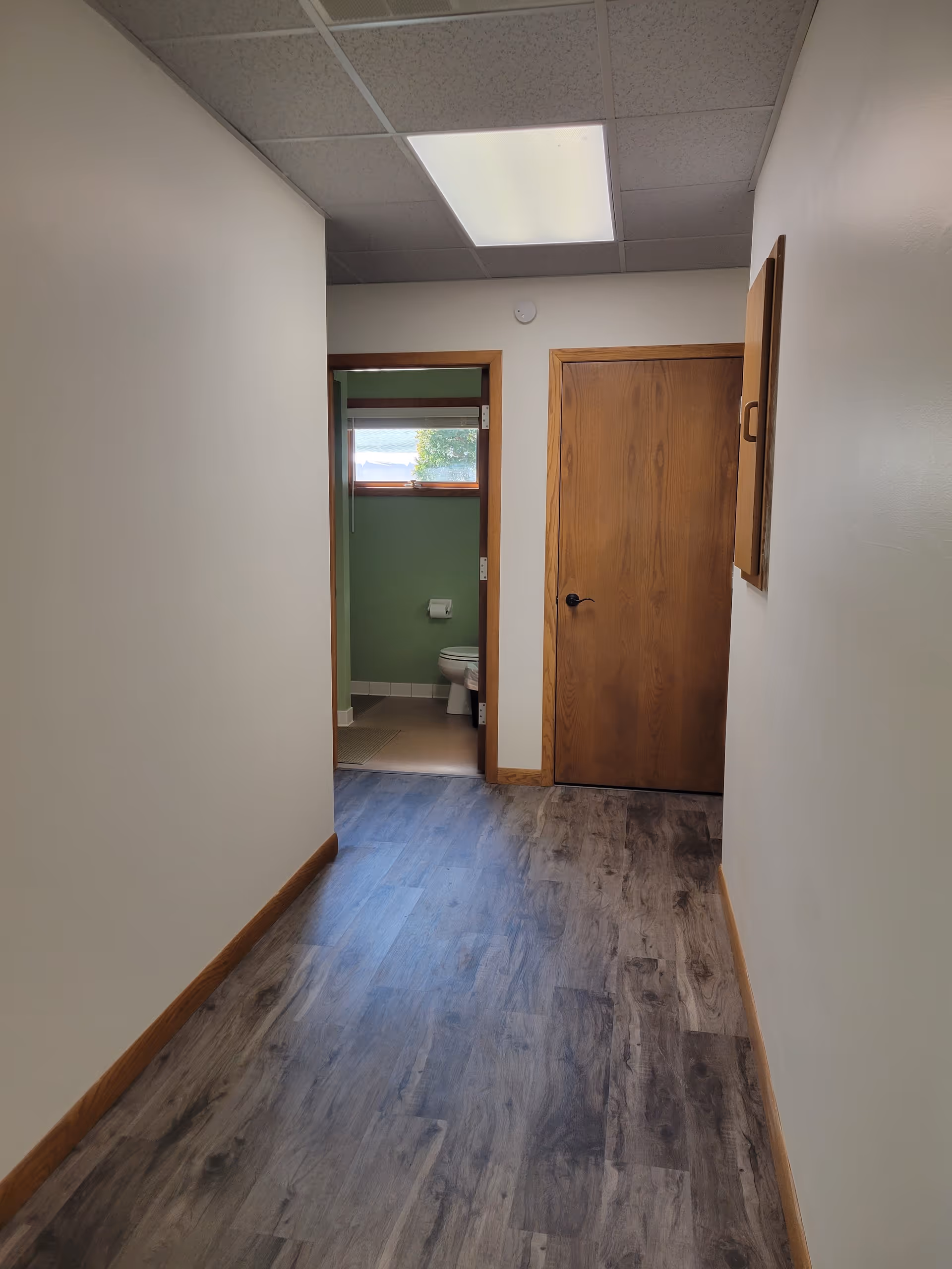 Narrow hallway in a senior care facility with a small bathroom visible at the end.
