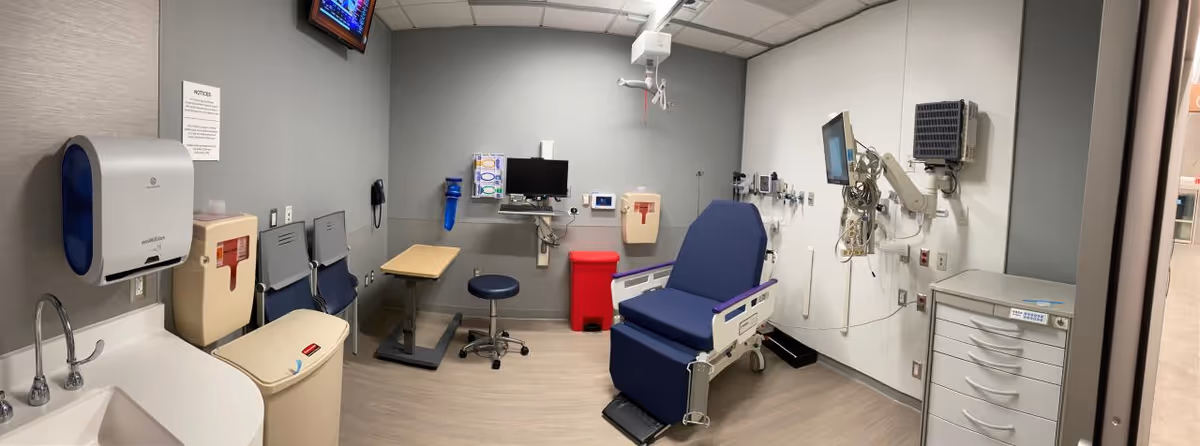 Interior medical procedure room with an exam chair, monitors, and wall-mounted equipment.