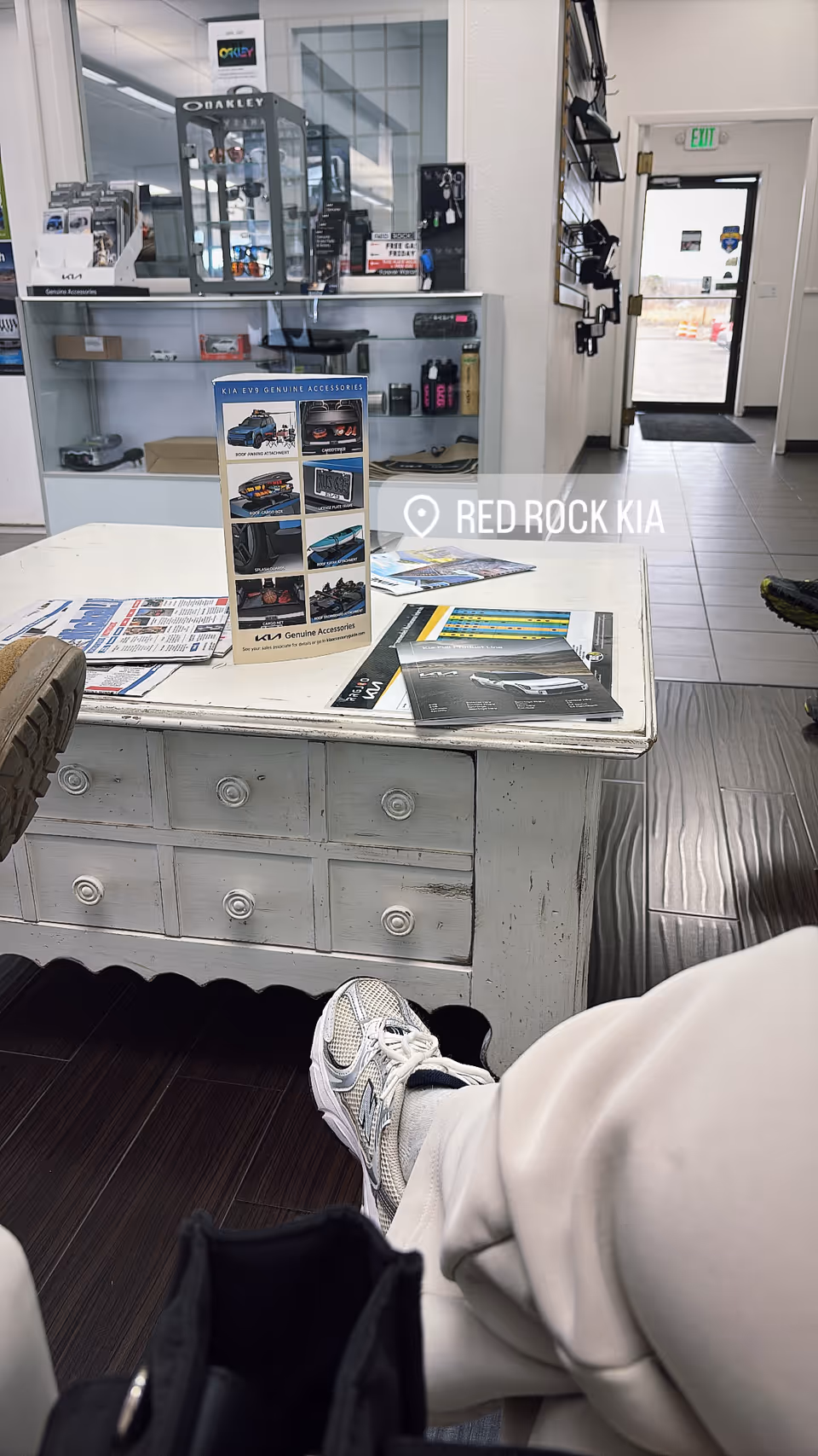 Interior of Red Rock Kia Parts Department showroom with shelves, brochures, and a seated shopper.