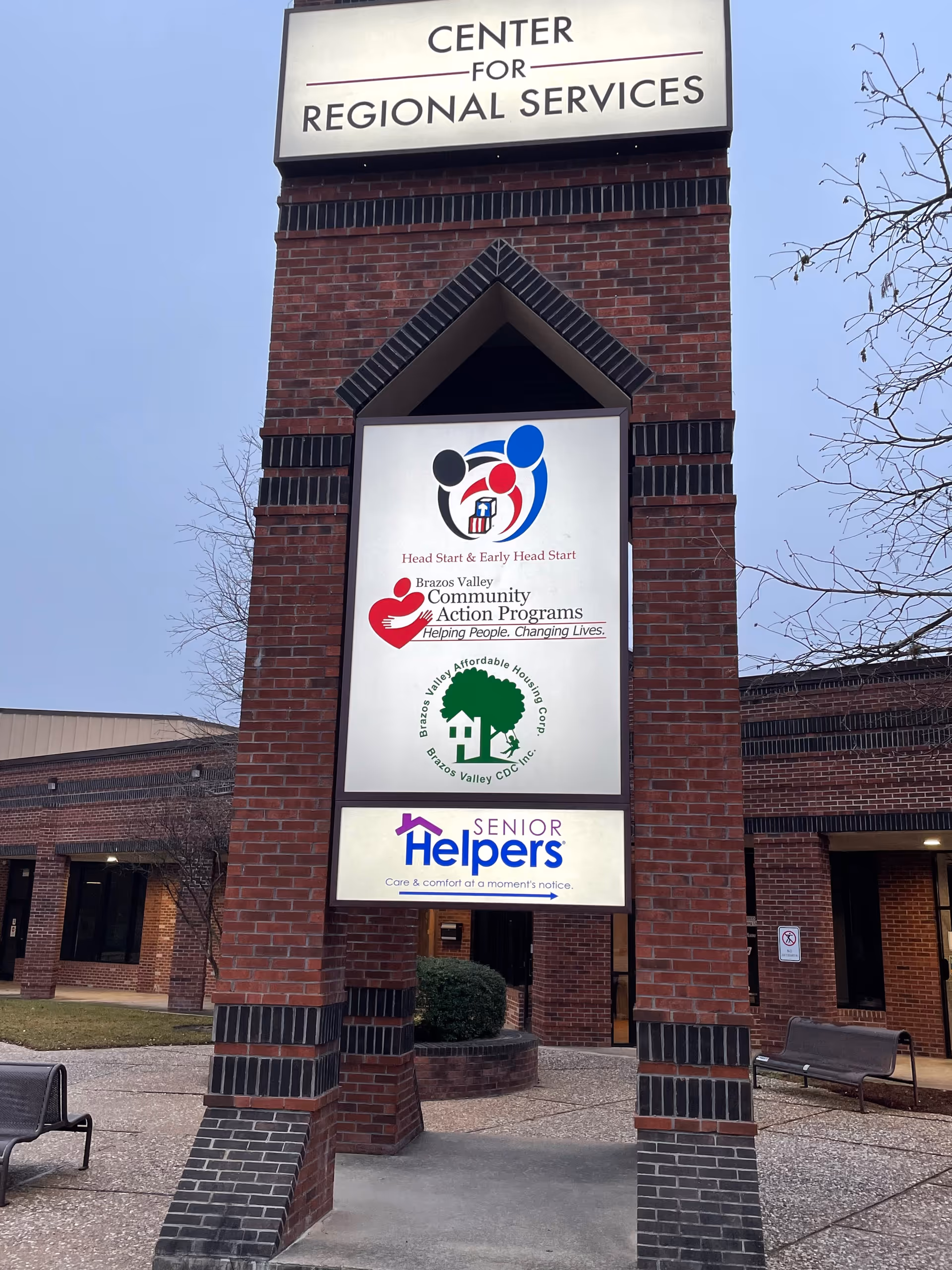Brick sign tower outside a building showing Senior Helpers and community program logos.