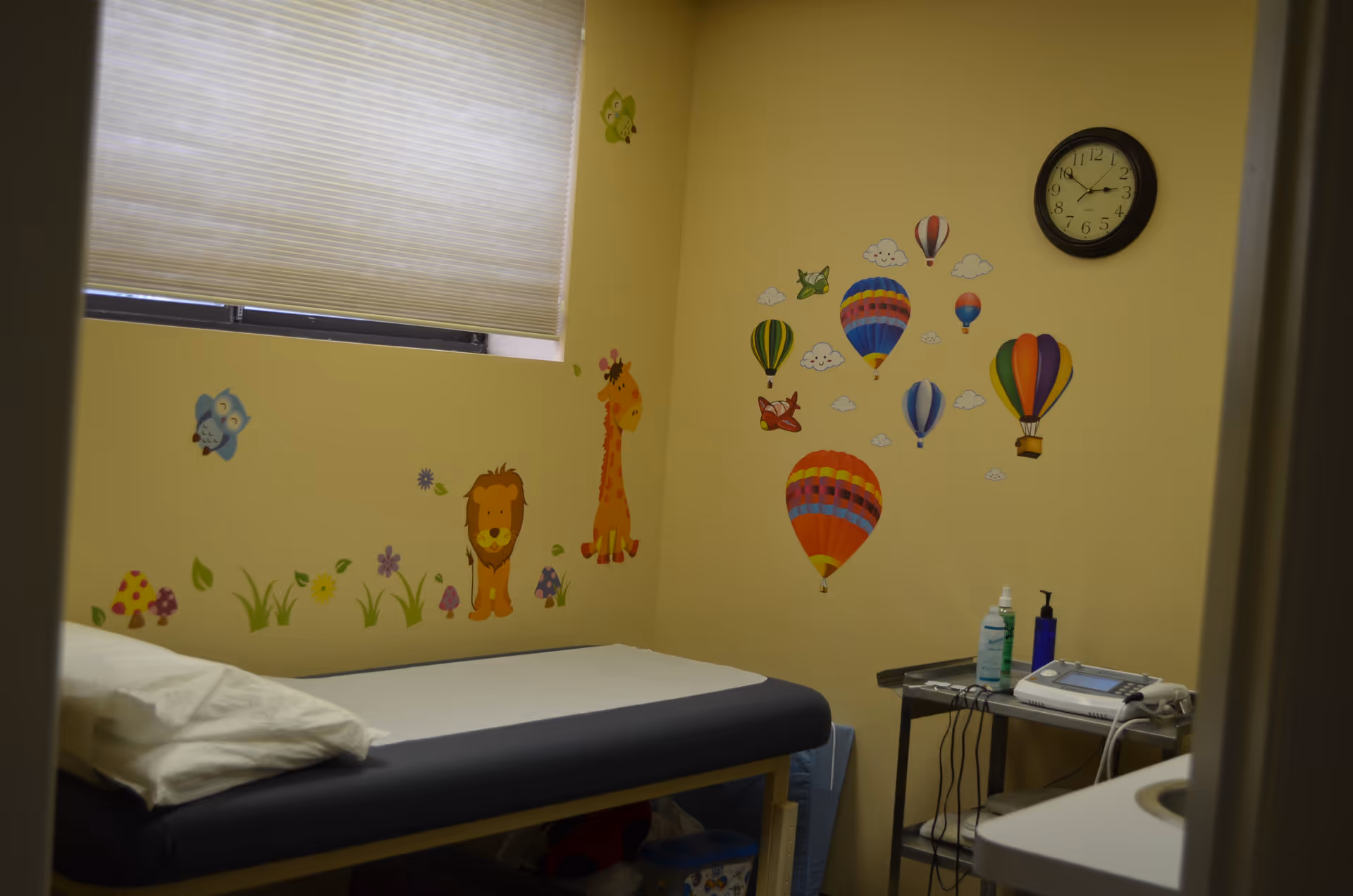 Bright treatment room with a single bed, playful wall decals, and medical devices.
